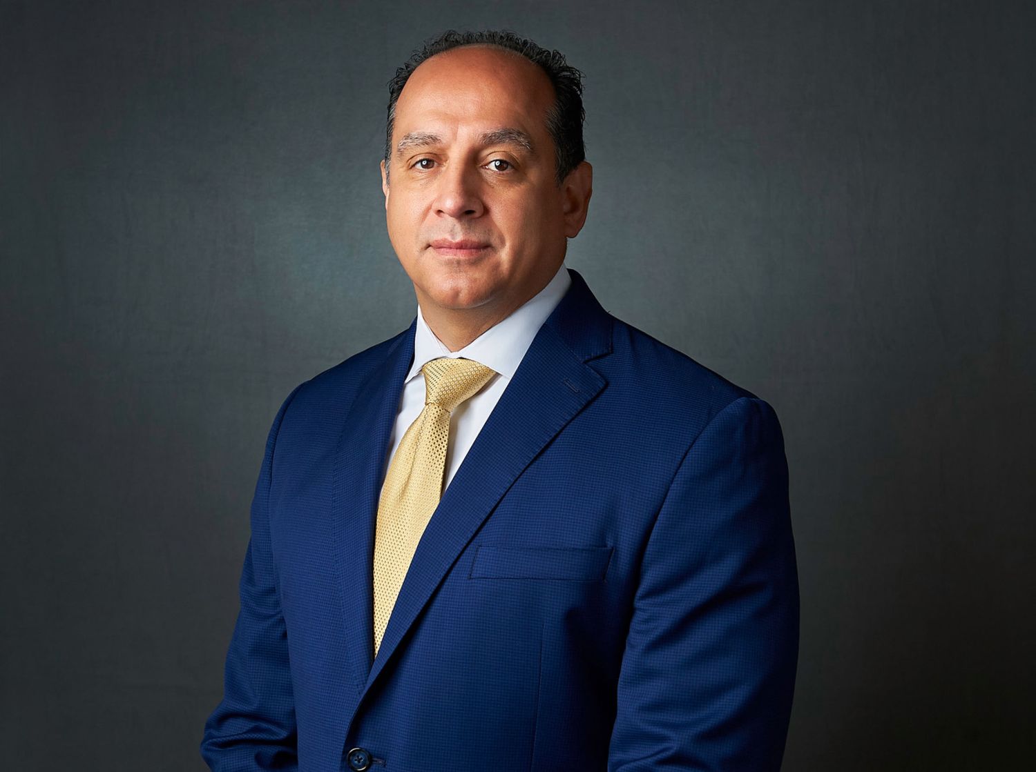 Professional businessman in blue suit and gold tie posing for formal corporate headshot portrait.