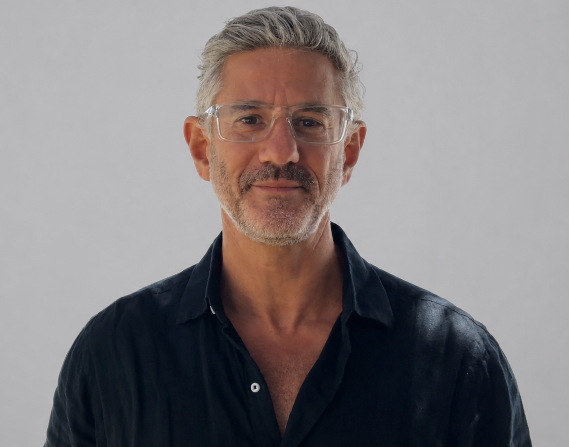 Middle-aged man with gray hair and glasses wearing a dark shirt against a light gray background.
