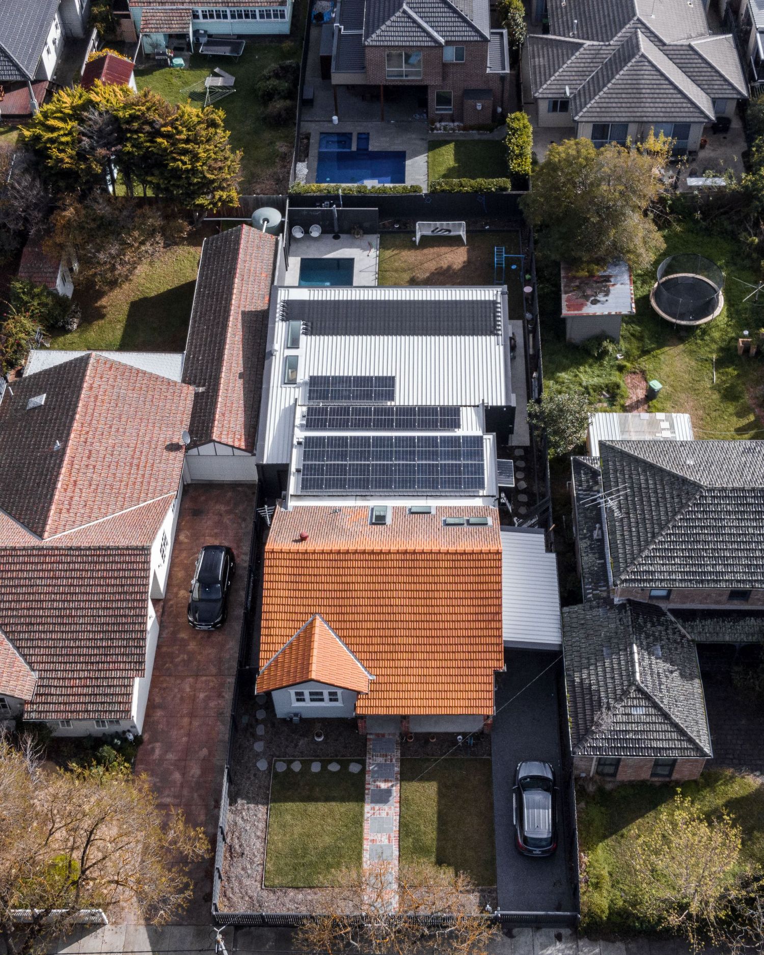 Aerial view of residential houses with solar panels on roofs and parked cars in suburban neighborhood driveways.
