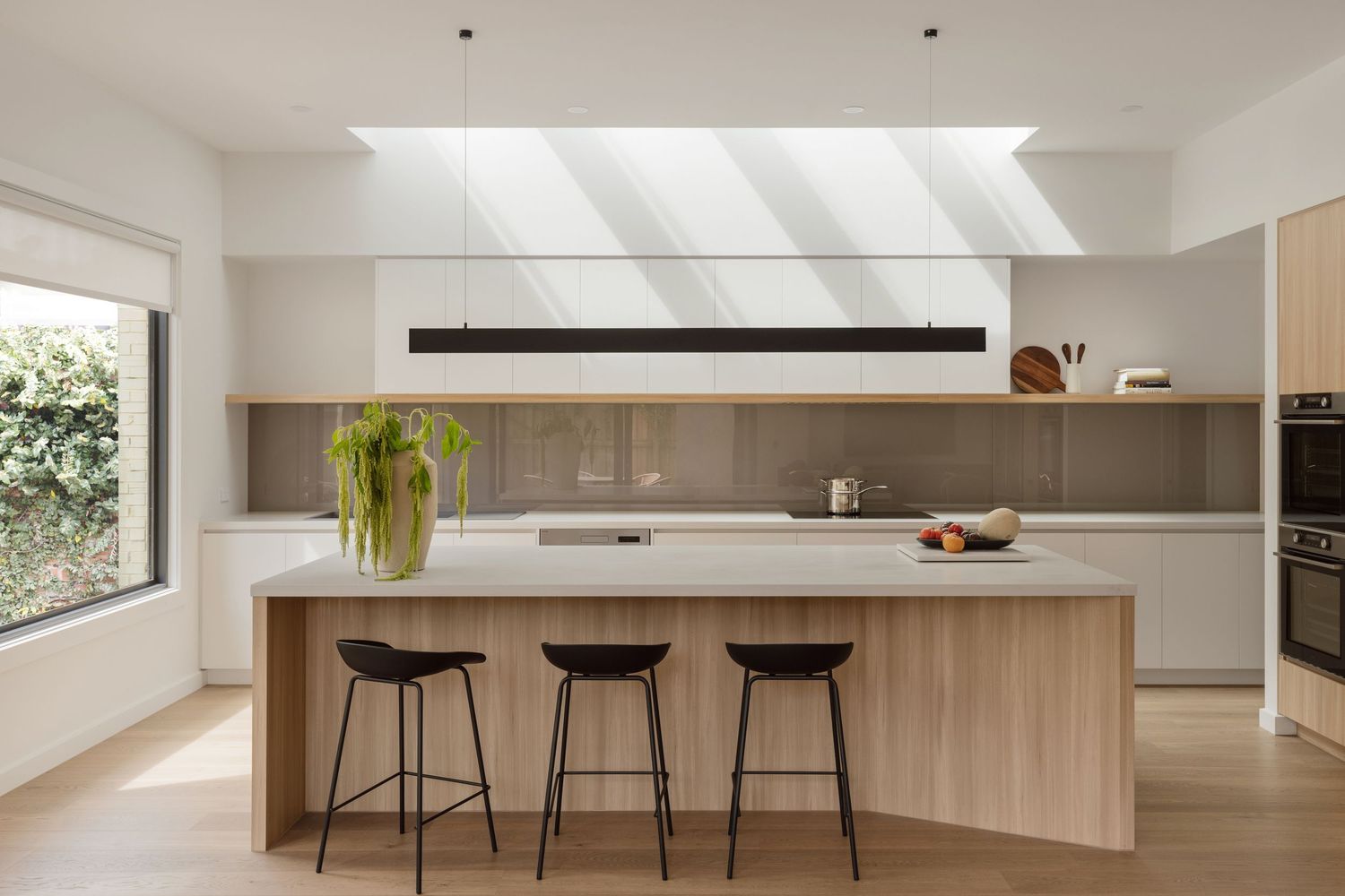 Modern minimalist kitchen with wooden island, skylight windows, black bar stools and sleek white cabinetry.