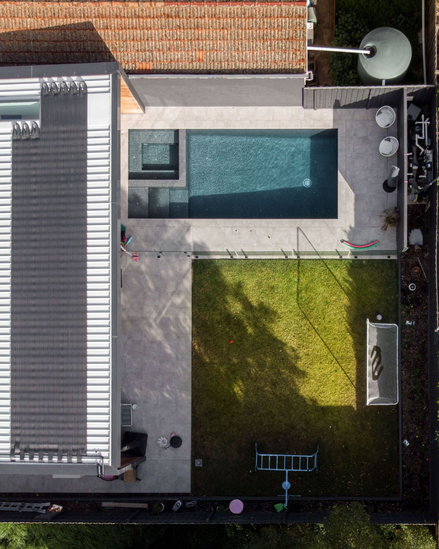 Aerial view of a modern backyard featuring a rectangular swimming pool, concrete patio, and green lawn area.