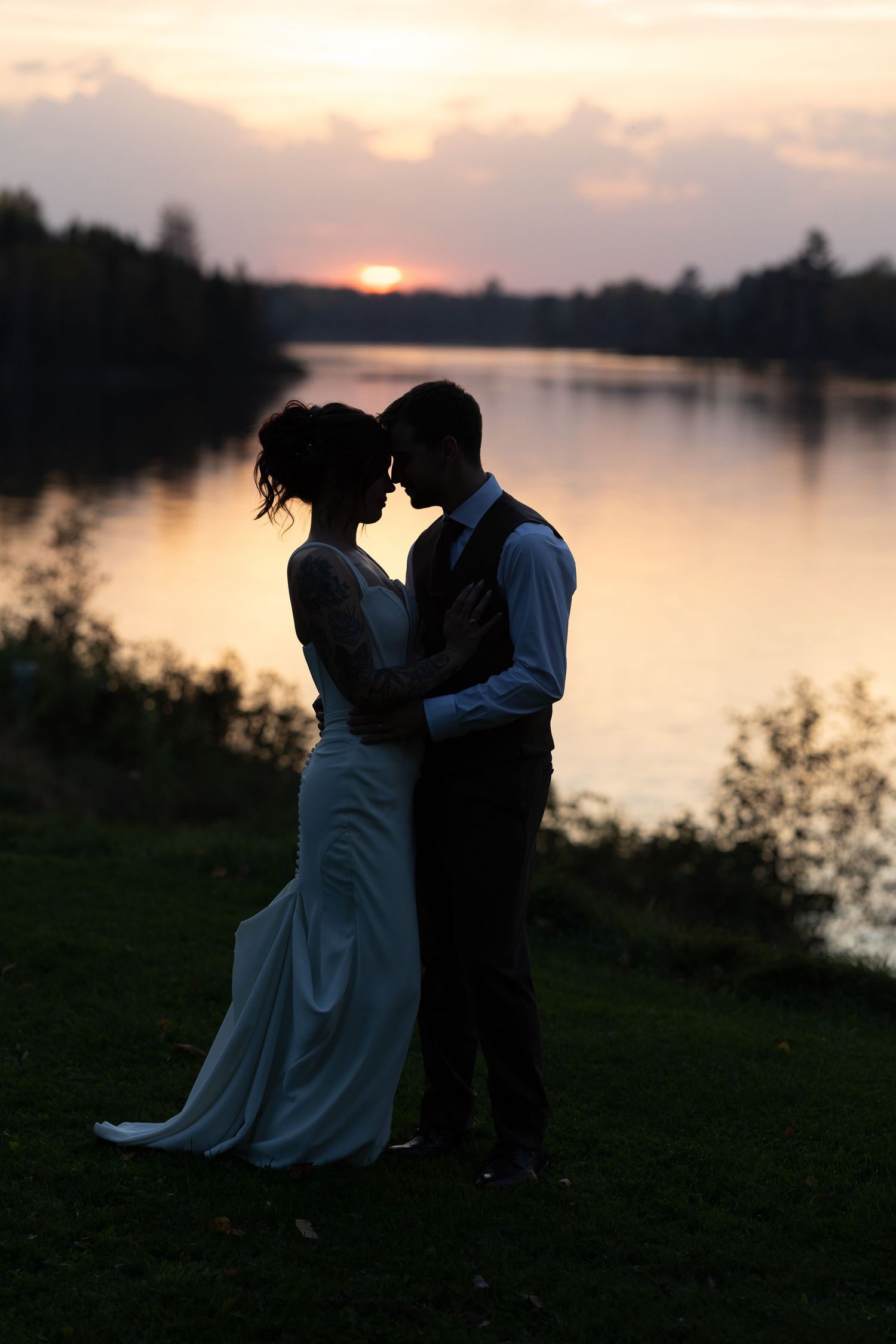 A romantic silhouette of a couple embracing by a serene lake at sunset creates a dreamy atmosphere.