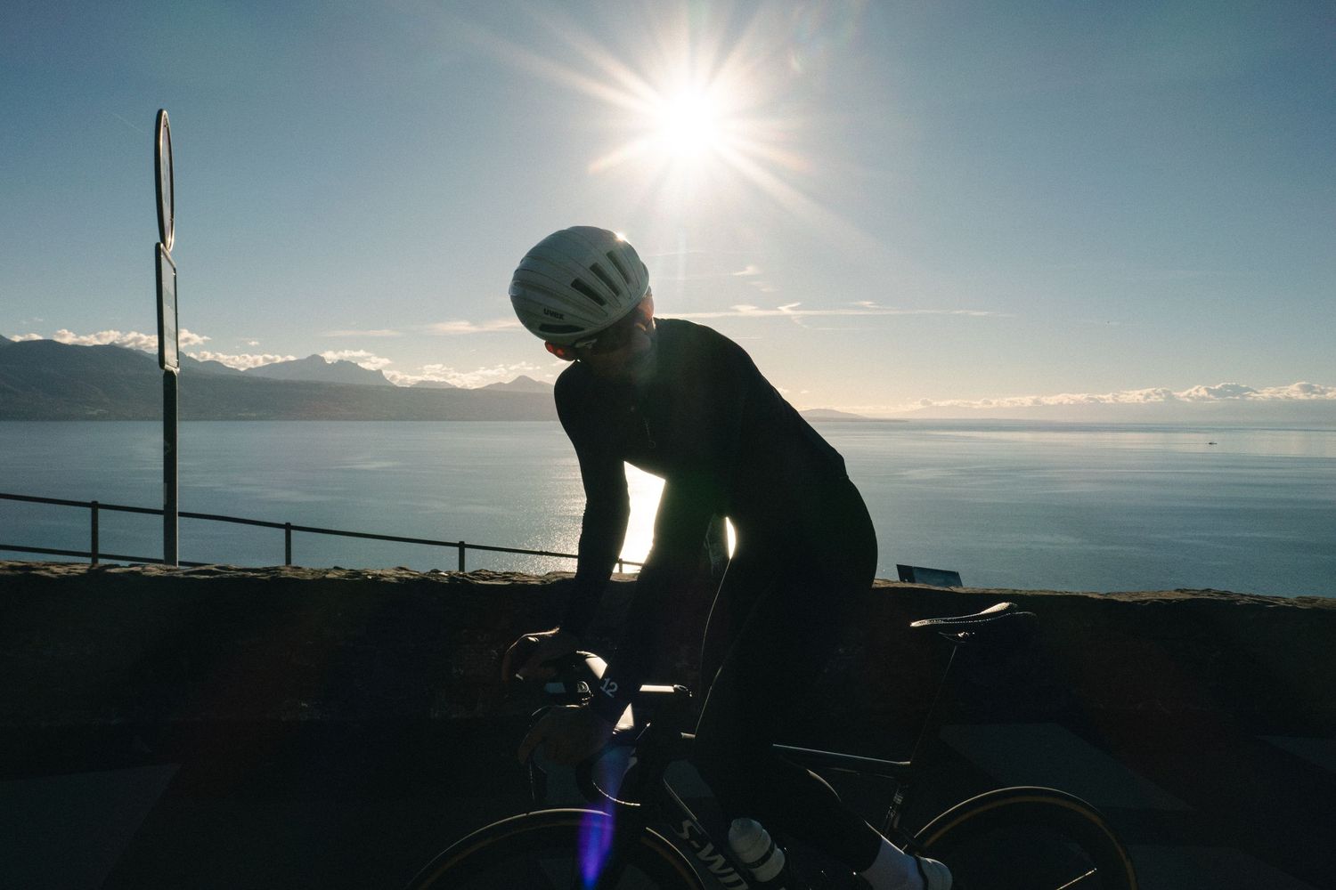 Cyclist silhouetted against a bright sunburst during a scenic coastal ride at sunset.