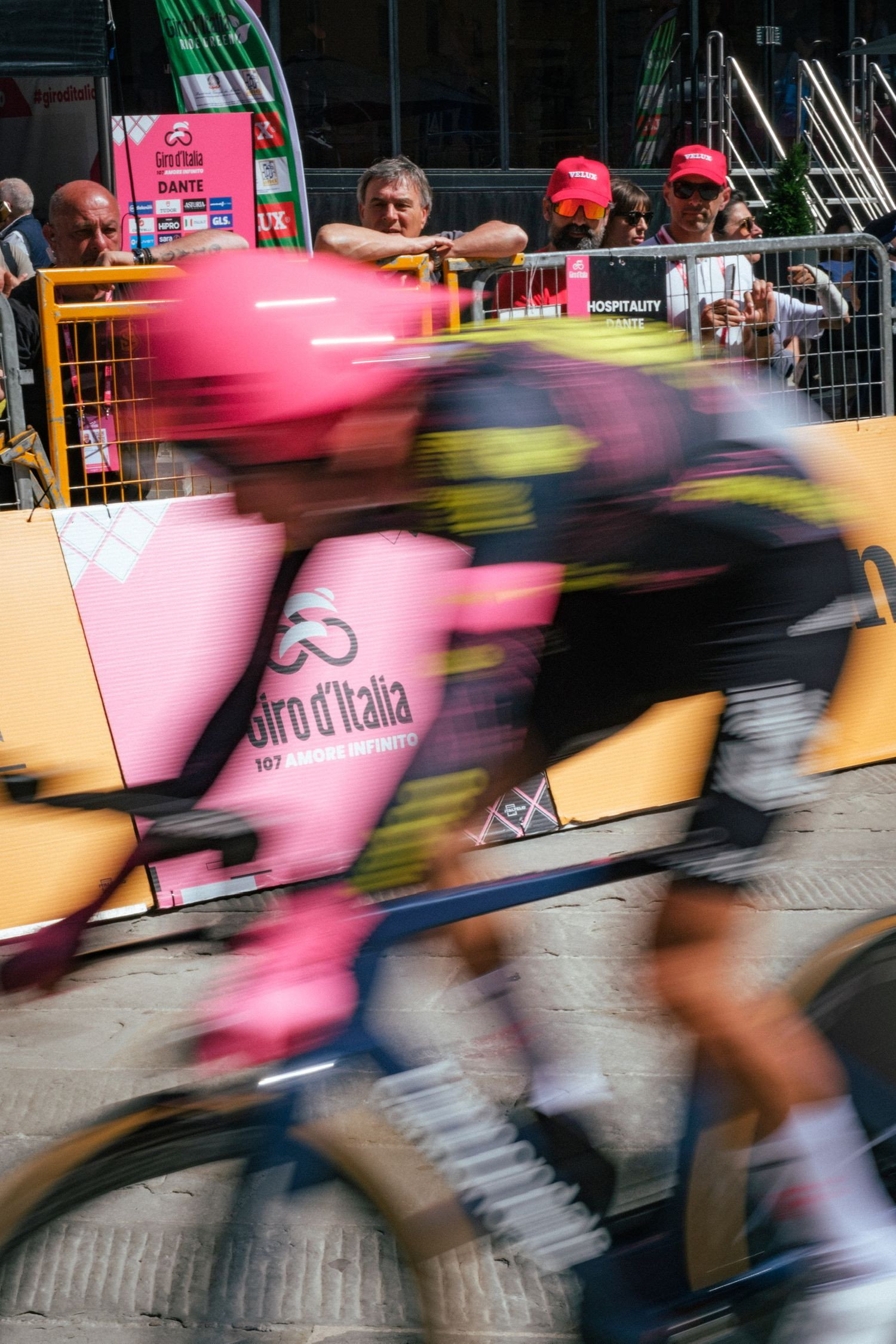 Motion blur captures cyclists racing in pink jerseys at high speed during the Giro d'Italia cycling competition.