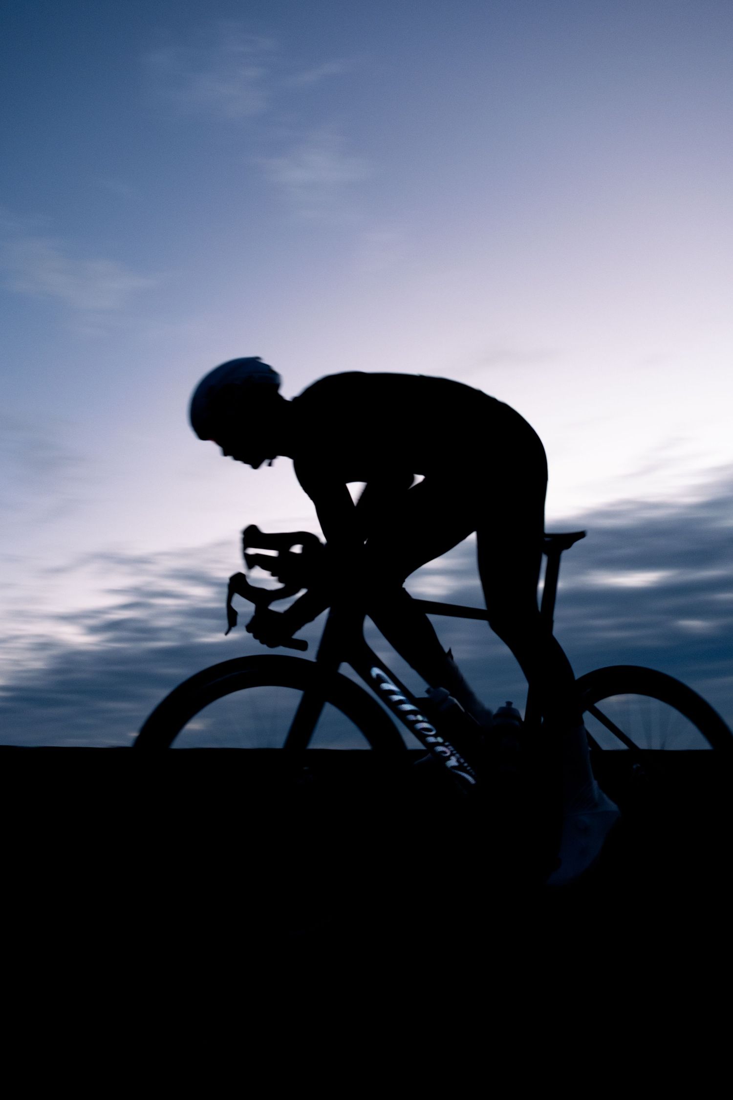 Silhouette of cyclist on racing bike against dramatic sunset sky with blue clouds.