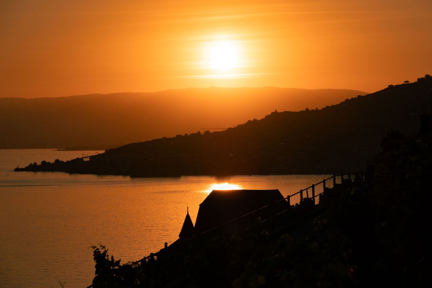 Scenic orange sunset over silhouetted coastal mountains and water with dramatic sky and warm glowing sunlight.