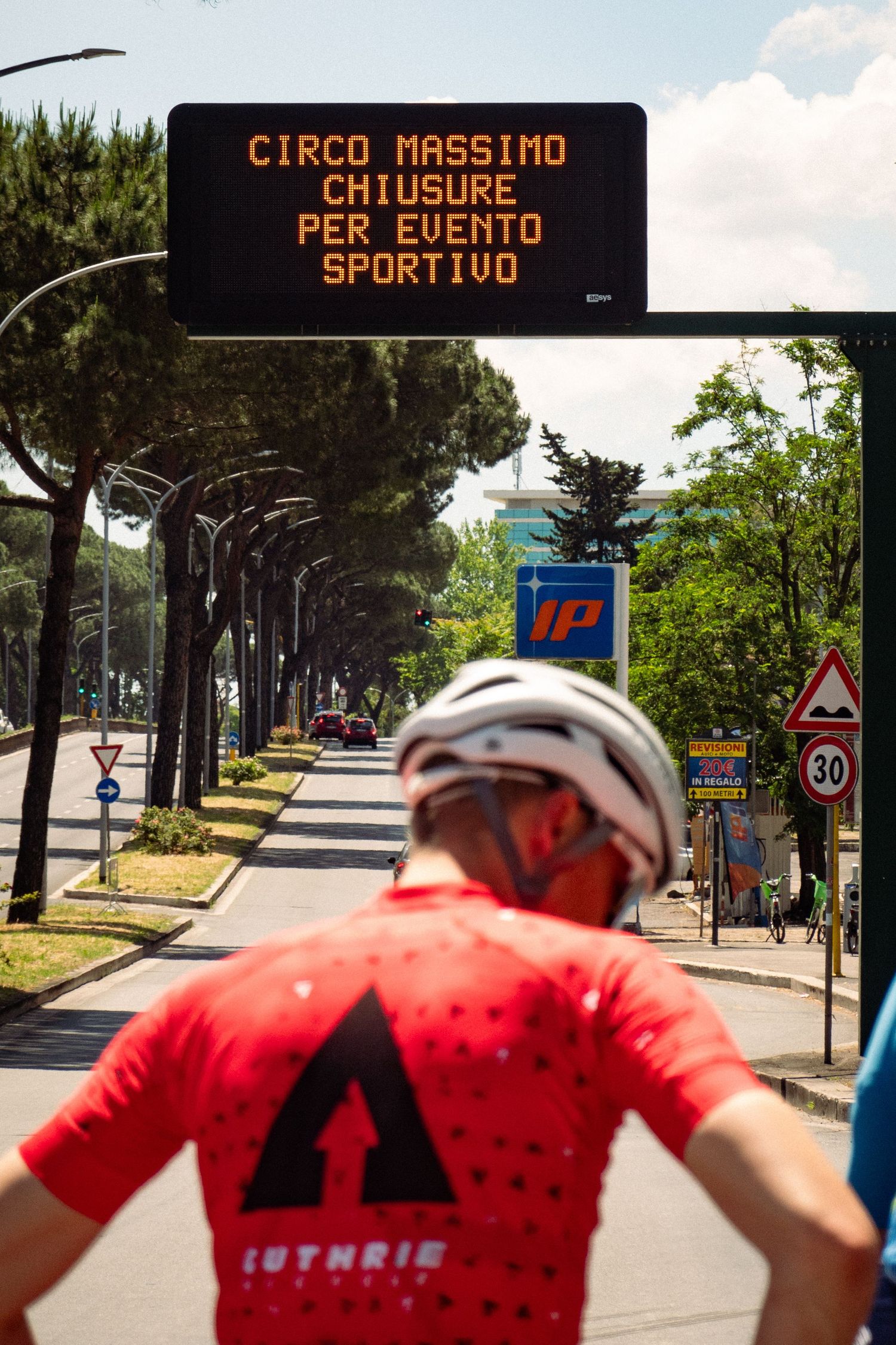Electronic road signs and tree-lined path along an Italian street on a sunny day.