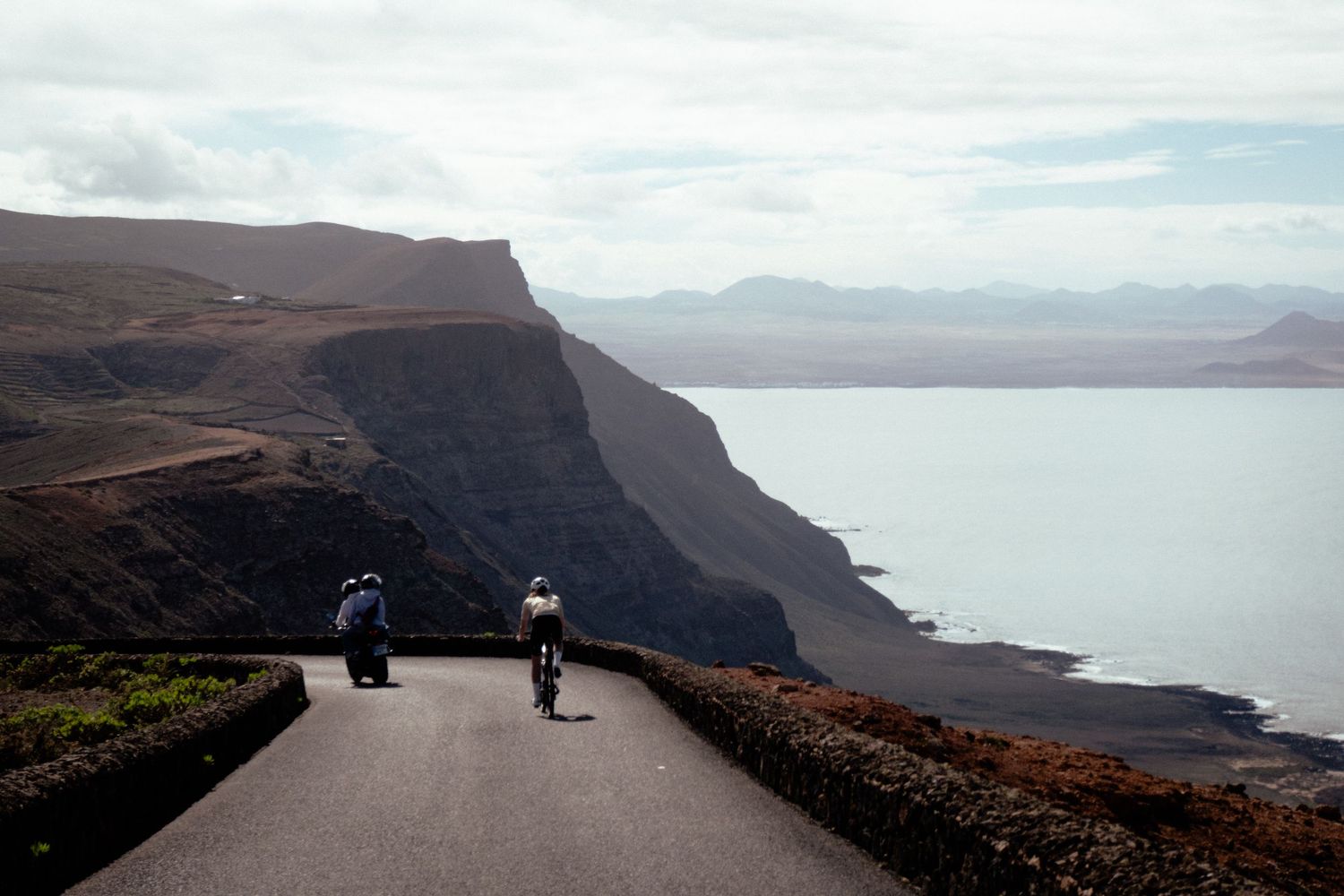 A scenic coastal road winds along dramatic cliffs overlooking the ocean on a cloudy day.