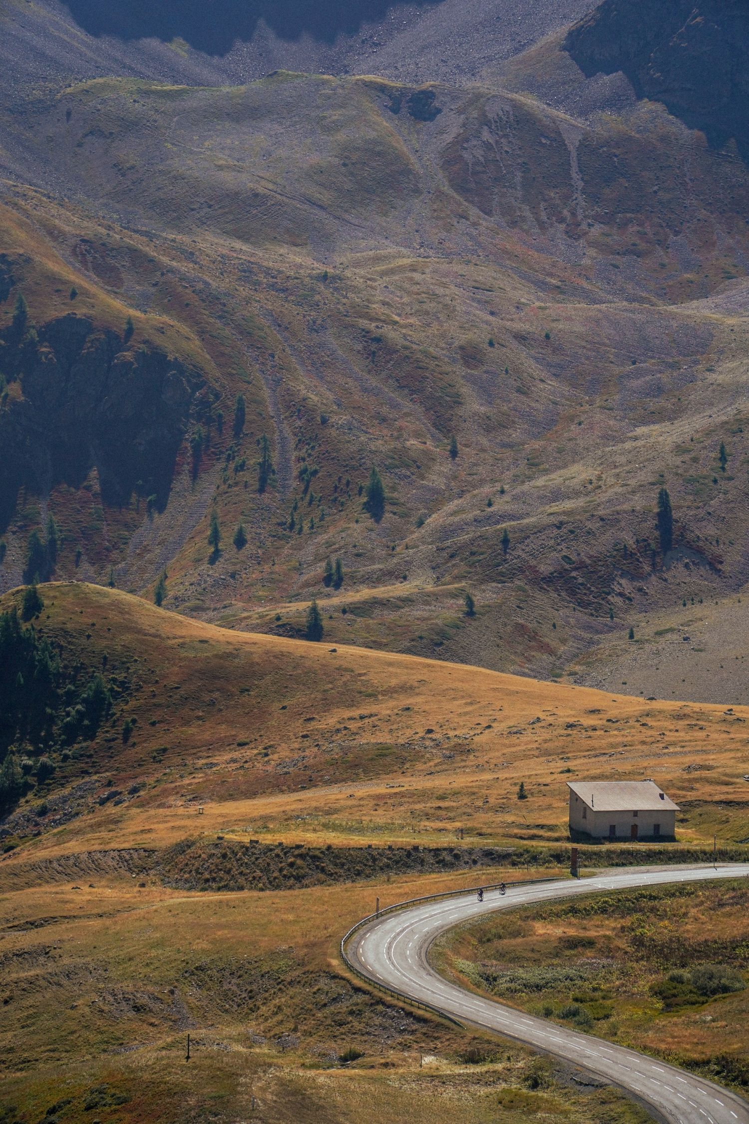Winding mountain road curves through rugged alpine terrain with dramatic mountain peaks in the background. Col du Galibier.