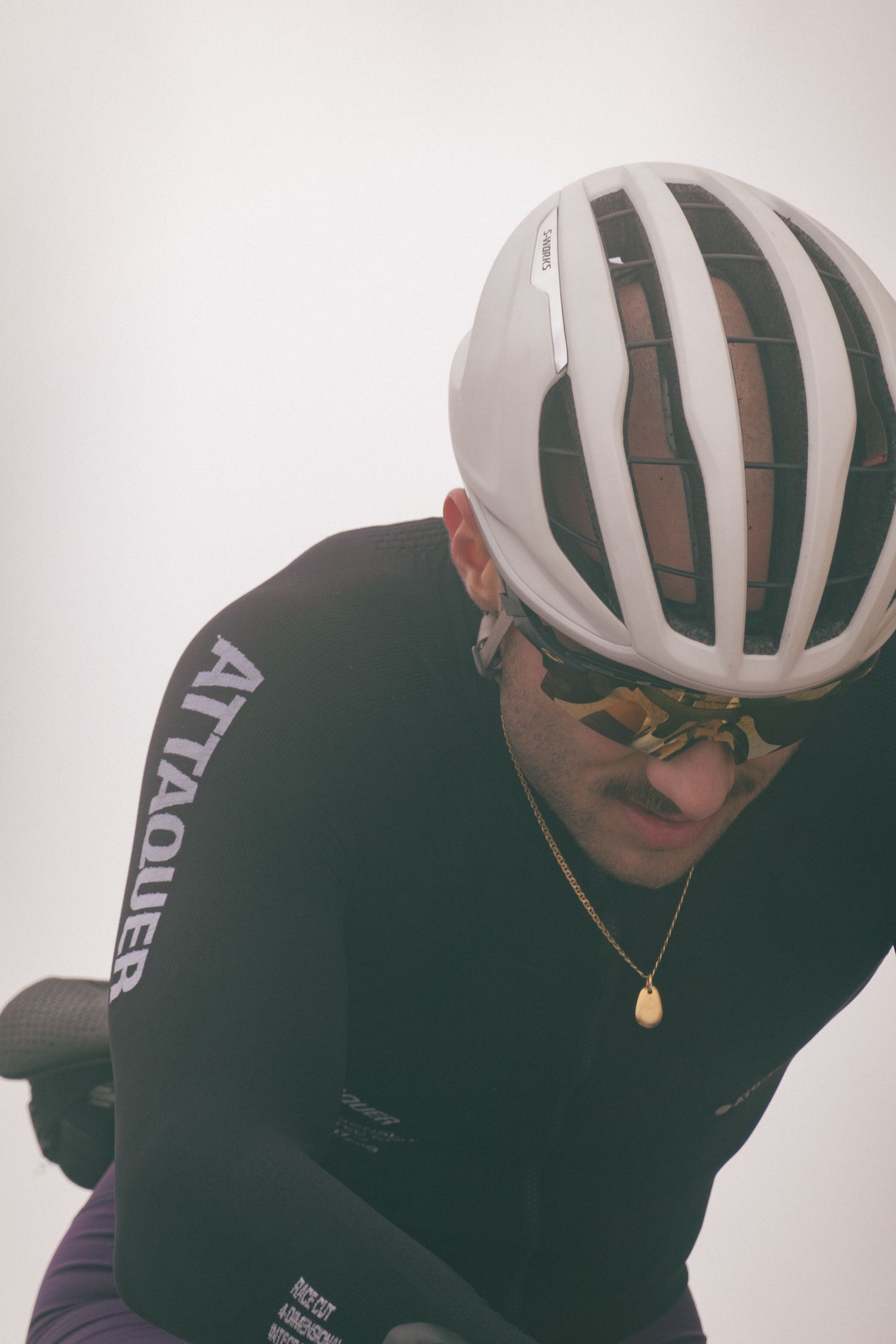 A cyclist in a white helmet and black jacket leans forward in an aerodynamic position while riding.