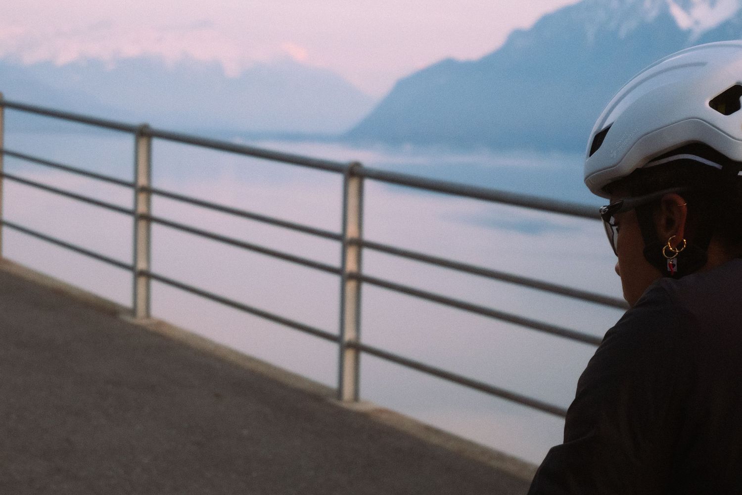 A cyclist rides along a scenic coastal path with white railings and ocean views at sunset.