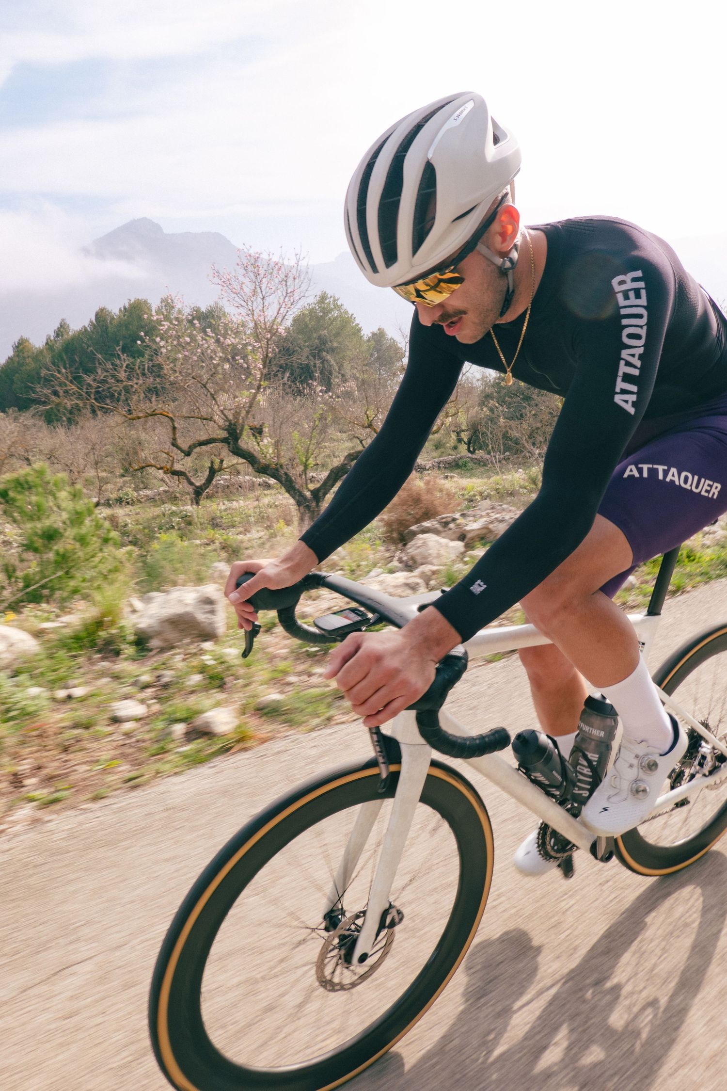 A cyclist in dark cycling gear rides a road bike on a scenic mountain path during a training session.