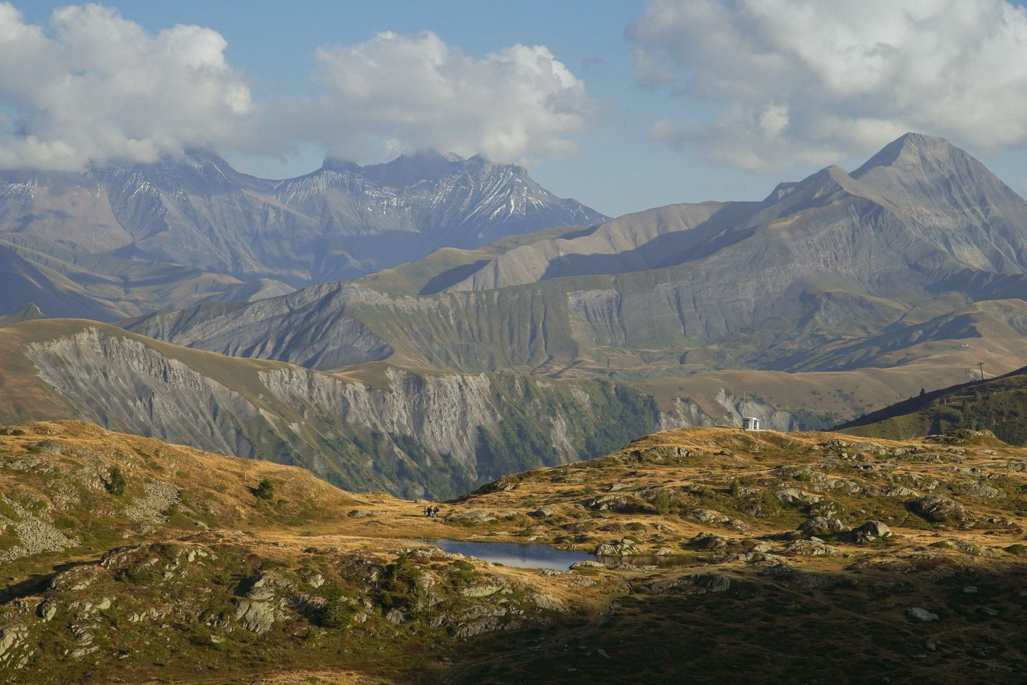 Panoramic mountain landscape with rugged peaks and golden autumn meadows in the French Alps under clear blue skies.