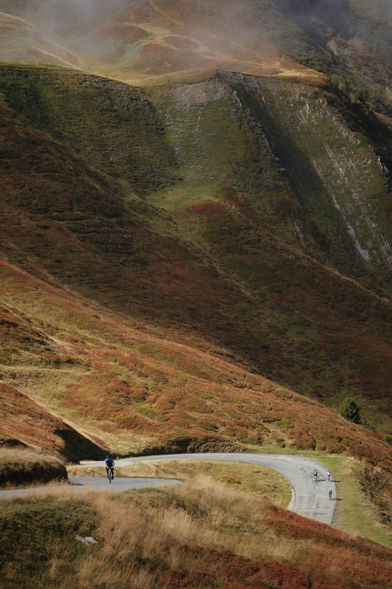 Winding mountain road curves through rugged terrain with autumn colors on the hillsides.