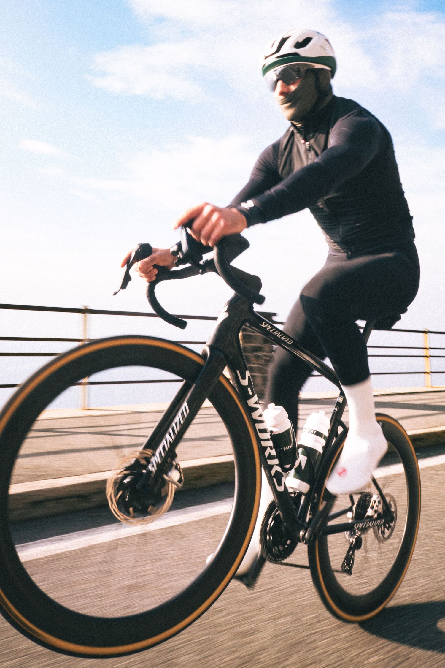 Cyclist in black riding a sleek racing bike with aerodynamic wheels along a boardwalk at sunset.
