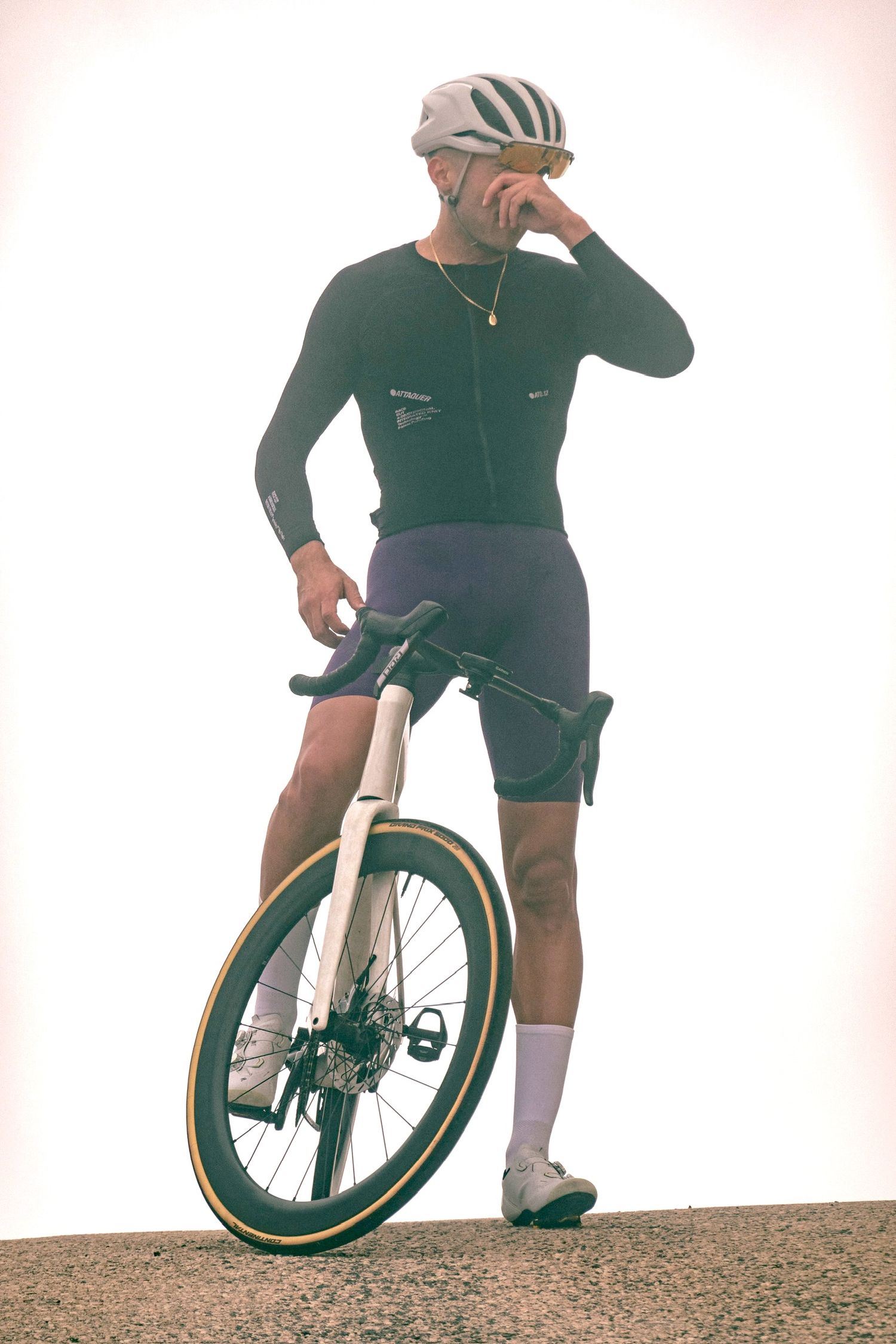 Cyclist in green and white riding gear performs tricks on a unicycle on a gravel surface.