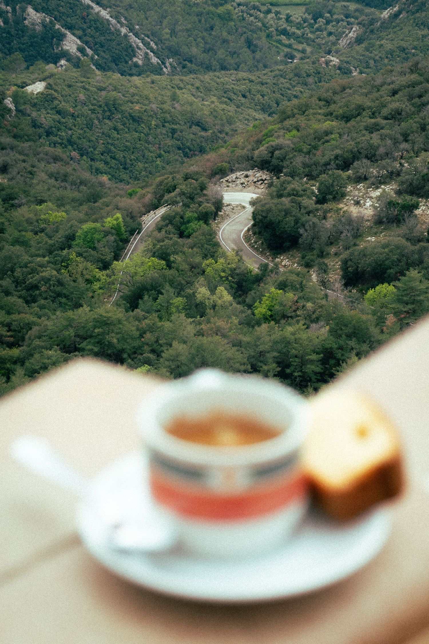 Mountain landscape with winding roads fading into a blurred foreground with coffee and cake.