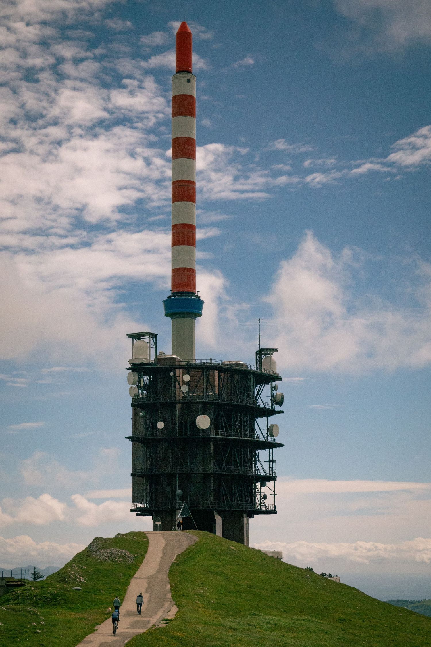 Communication tower and weather station stand atop a grassy hill against blue sky. Col de Chasseral in the Swiss Jura Mountains.