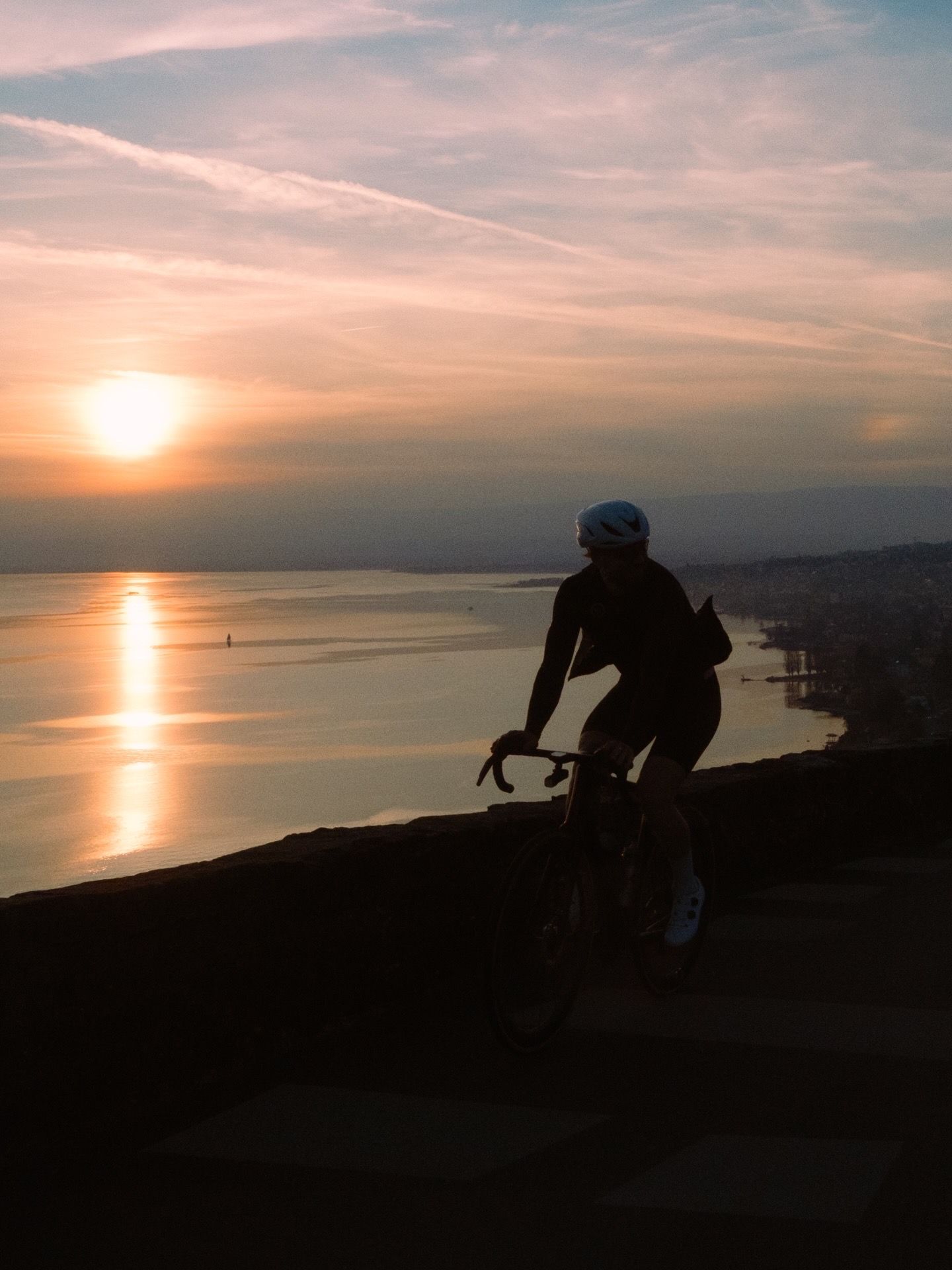 A silhouetted cyclist rides along a coastal ridge at sunset with dramatic orange sky and ocean views below.