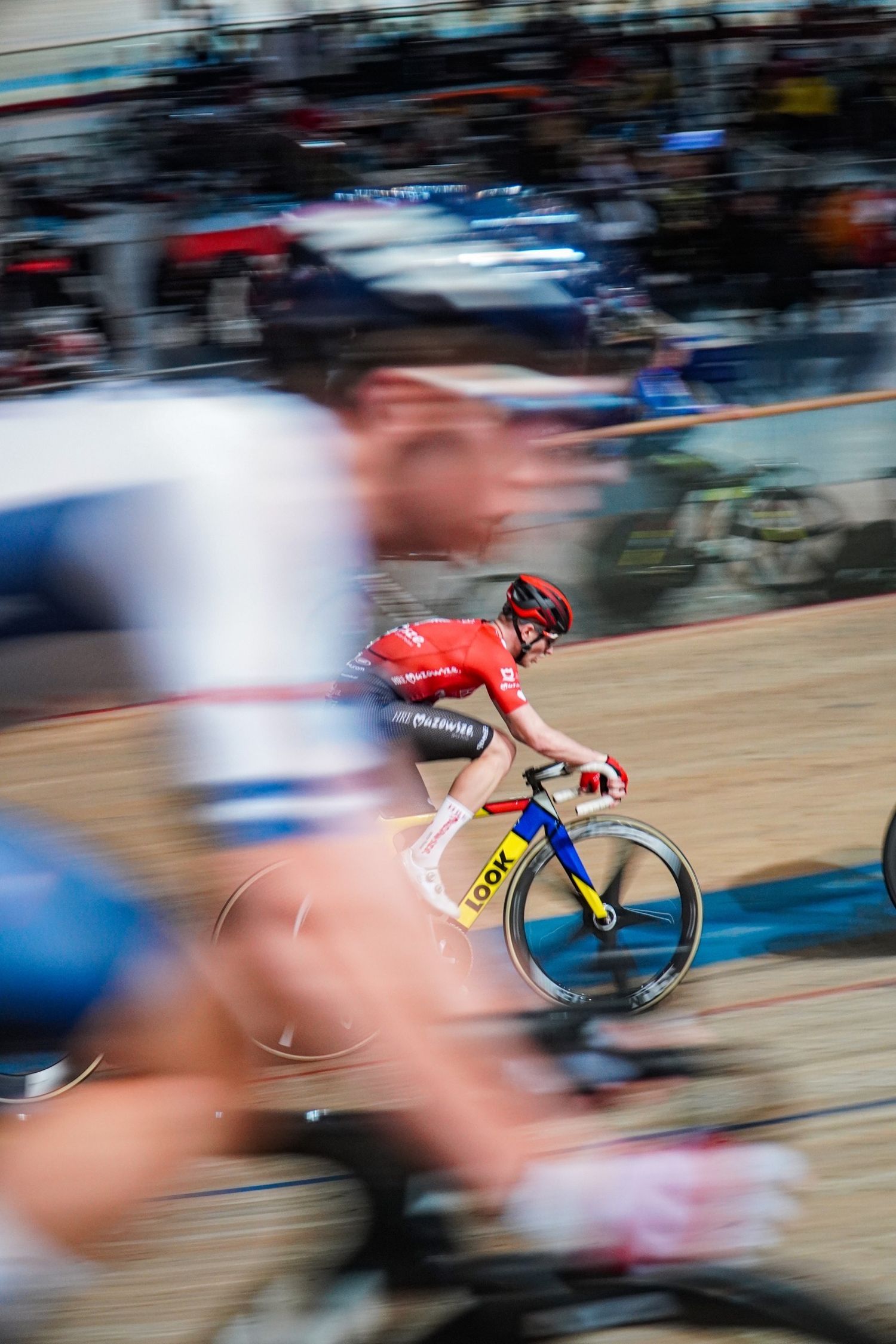 Motion-blurred cyclists race on a velodrome track during a competitive cycling event.