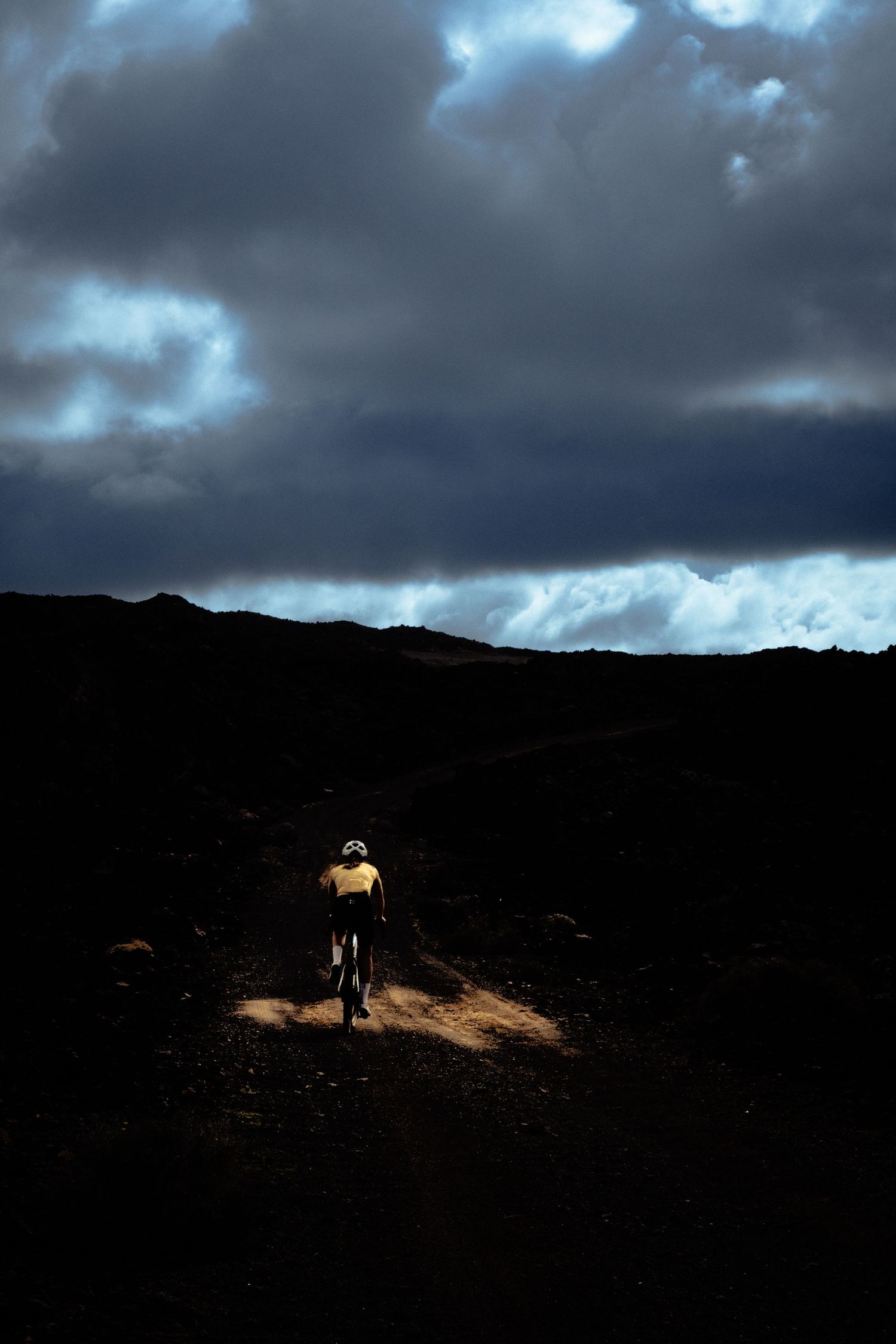A silhouetted figure walks along a dark mountain ridge against dramatic stormy clouds at dusk.