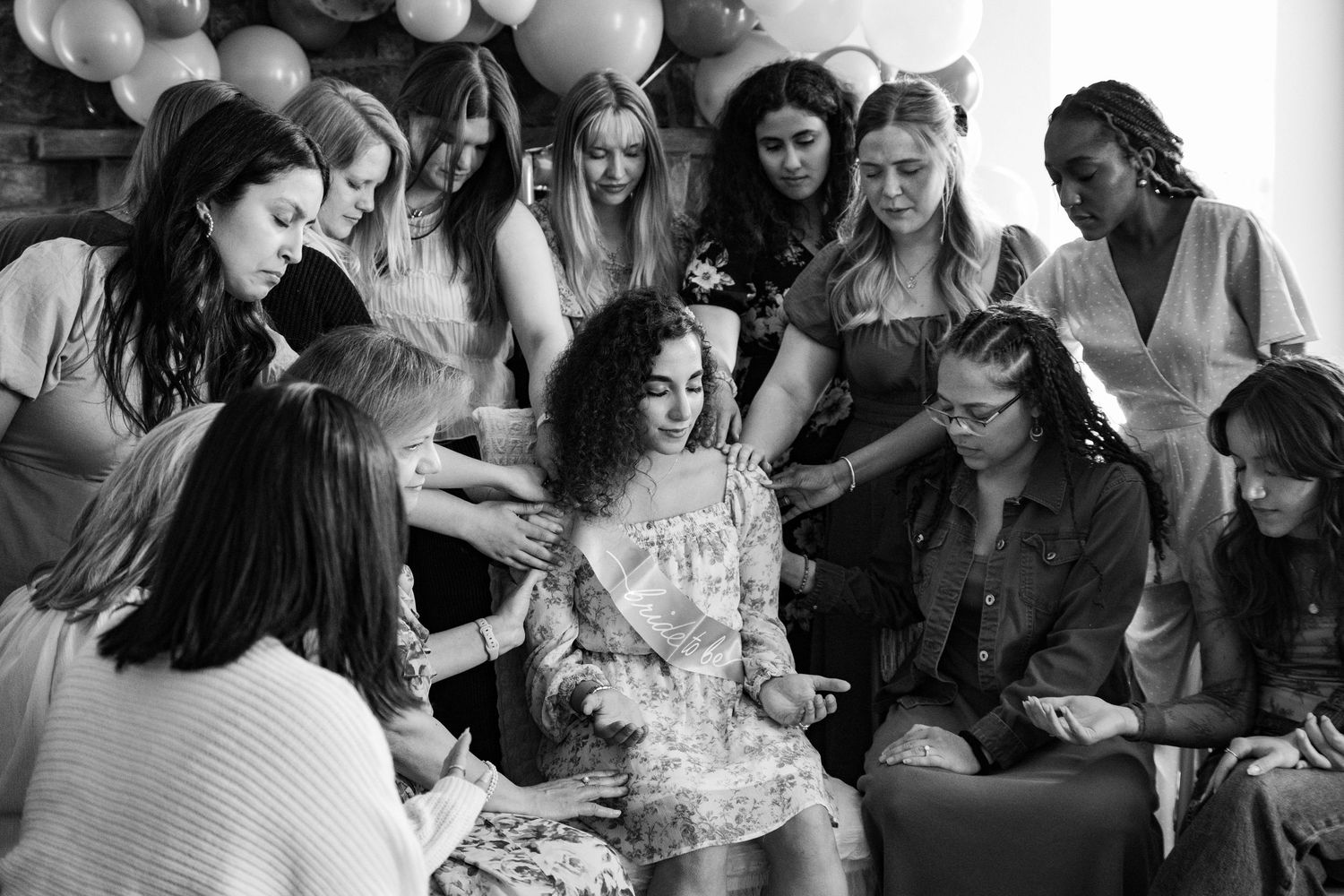 Sweet bridal party moment with friends placing their hands on the bride-to-be during the engagement celebration.