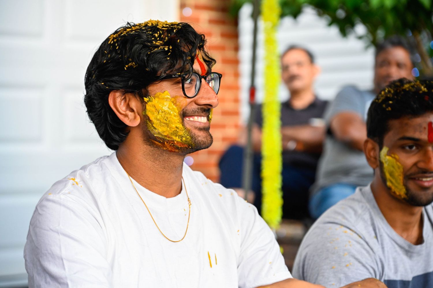 Groom smiling brightly with yellow haldi powder covering his face.