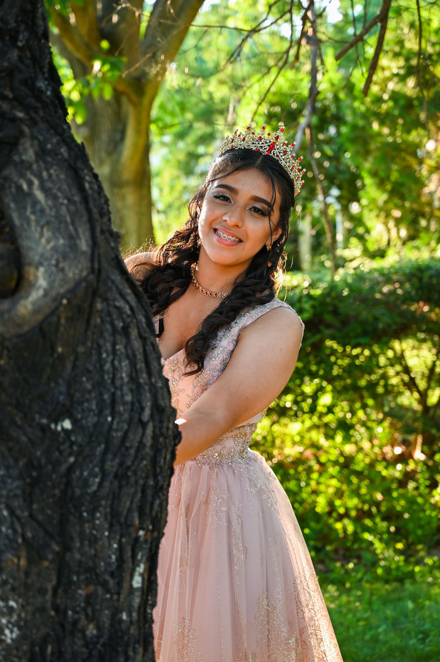 Playful portrait of the quinceañera peeking out from behind a tree during her photoshoot.