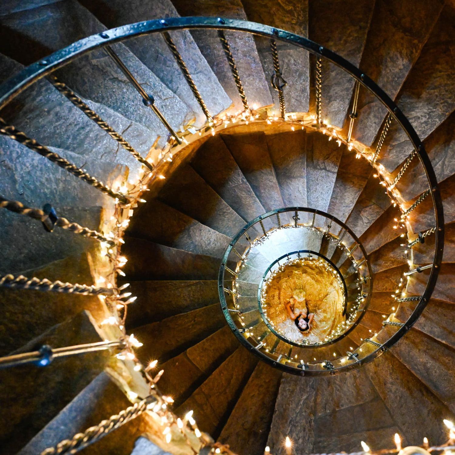 Dramatic portrait of the quinceañera laying beneath the spiral staircase at The Cloisters Castle
