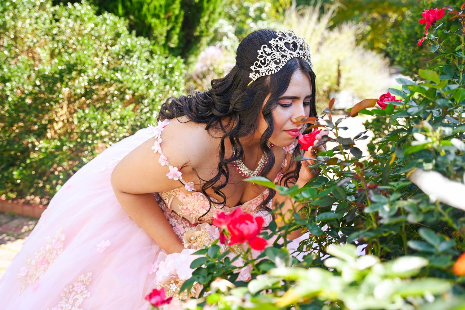 Sweet portrait of the quinceañera smelling roses in a beautiful garden setting.