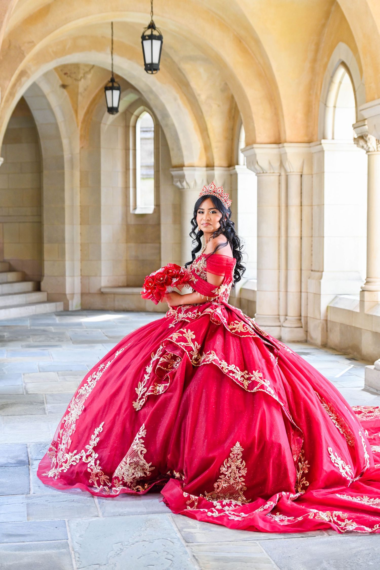 Elegant quinceañera portrait in a red dress at the Washington National Cathedral looking directly into the camera.