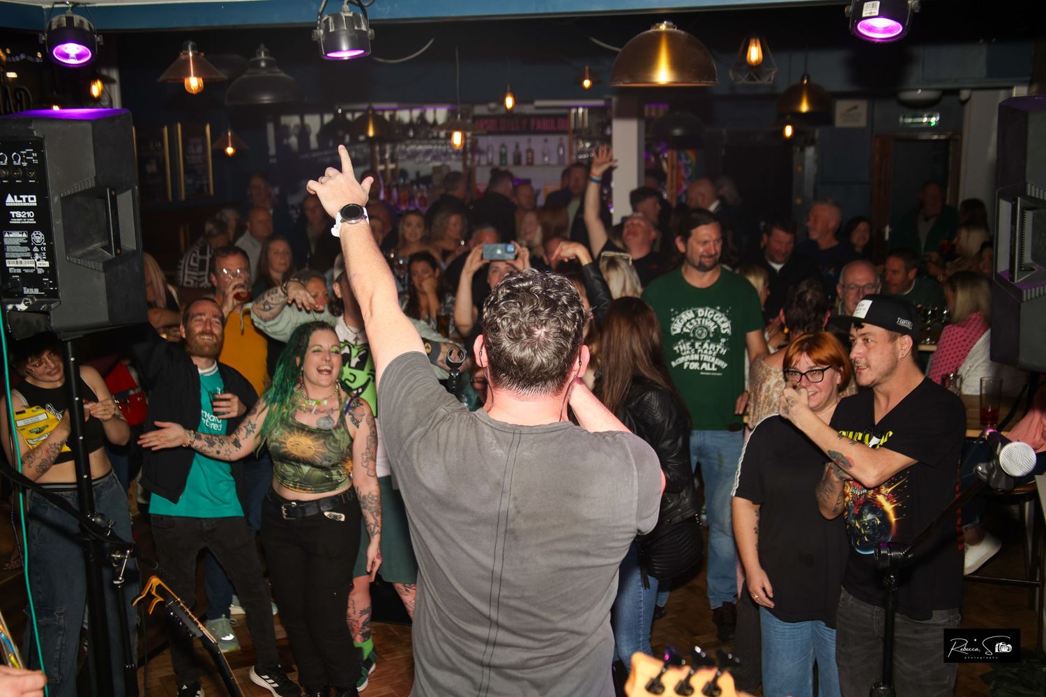 Energetic crowd at a small music venue with raised hands and colorful lighting.