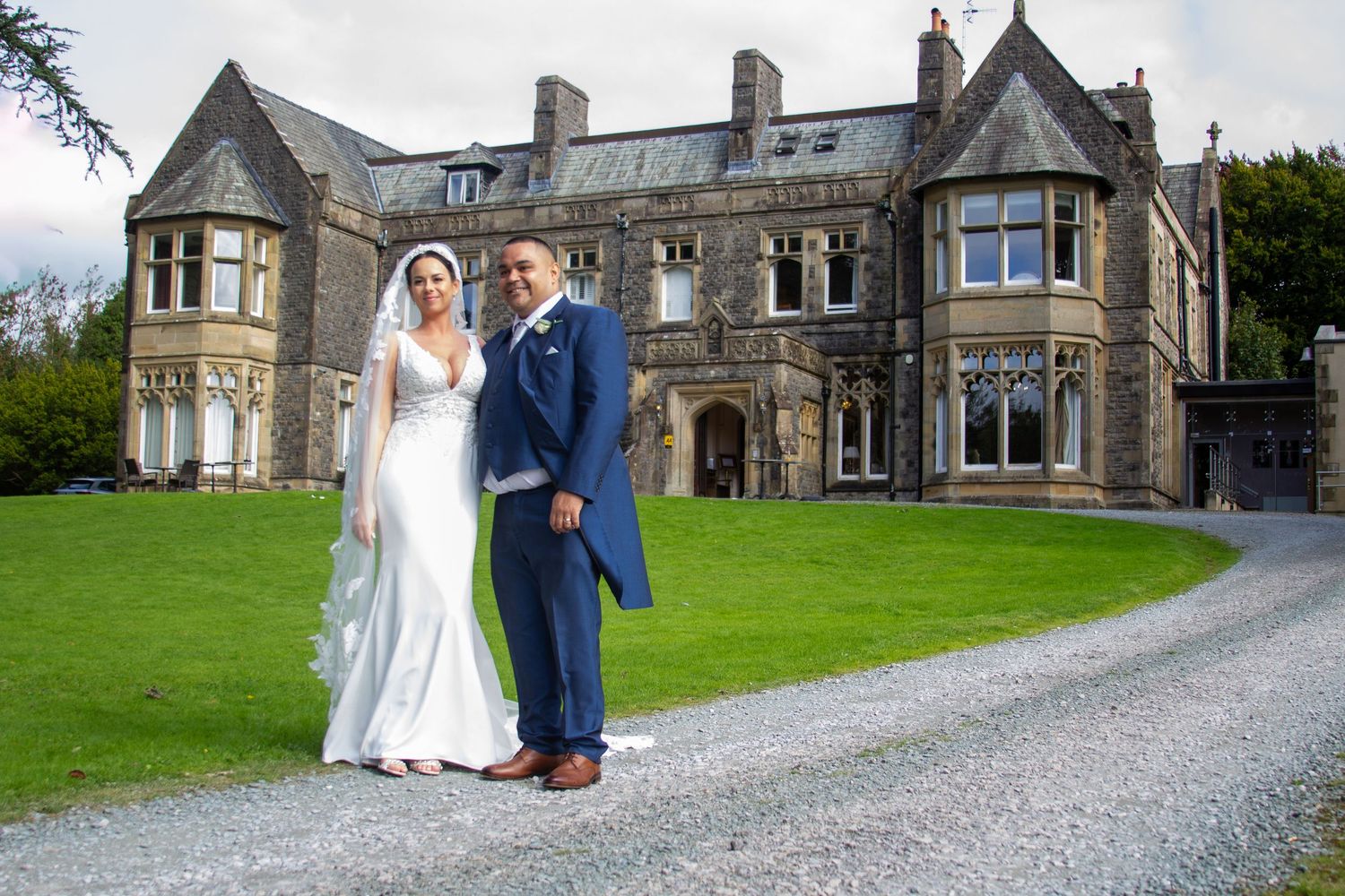 Newlyweds pose in front of grand stone manor house on their wedding day.