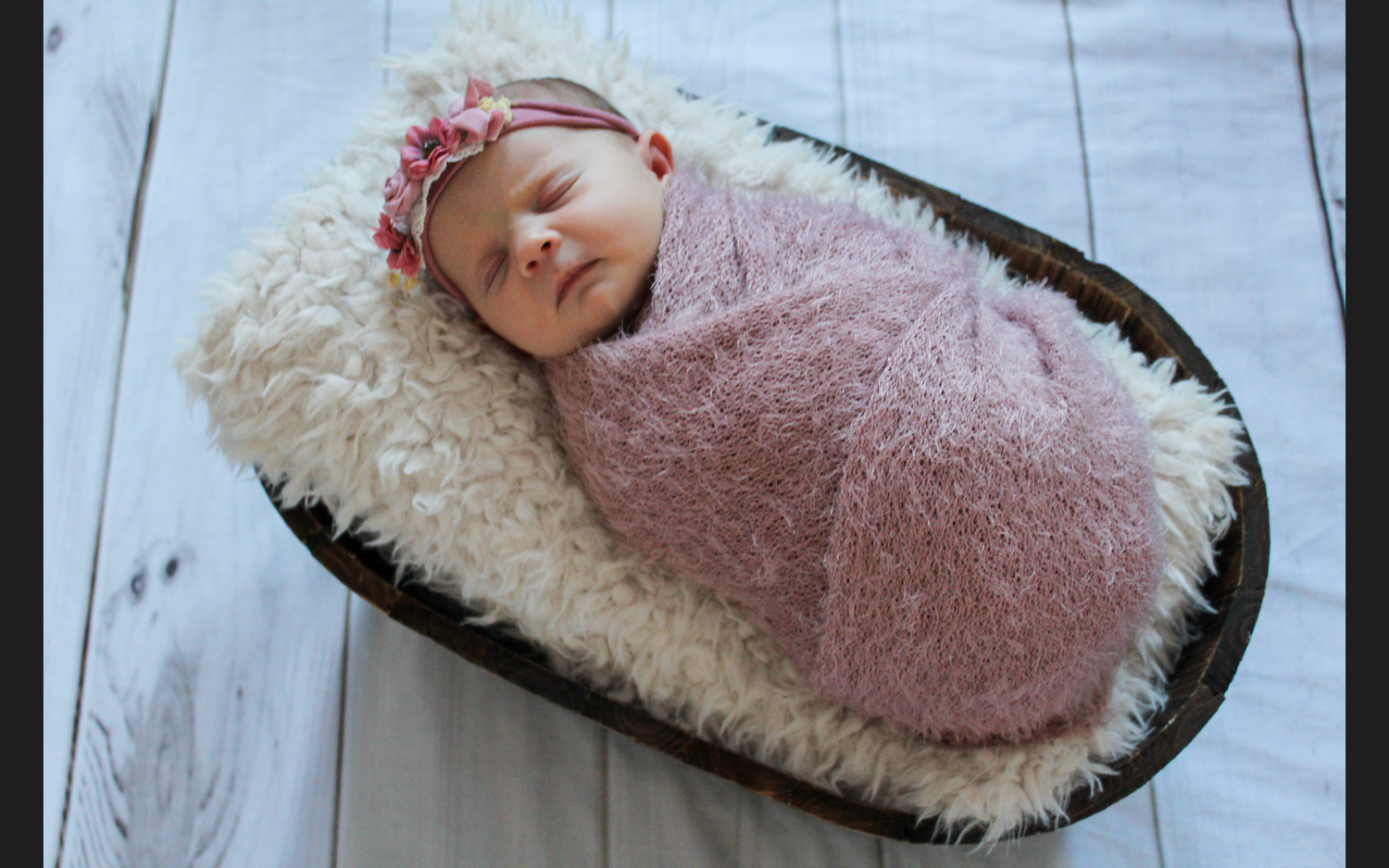 Sleeping baby in cozy sheepskin bassinet with pink blanket.