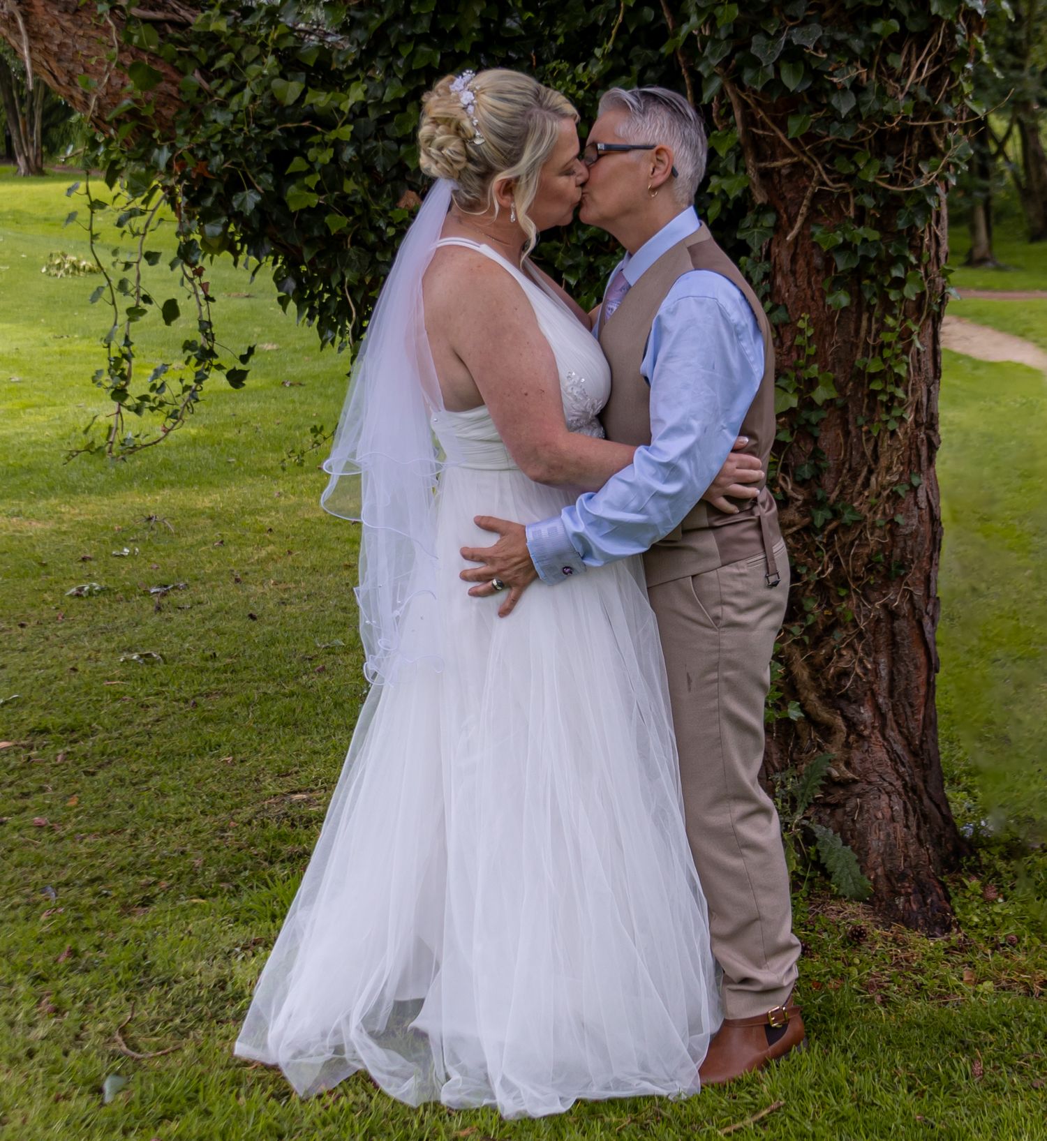 Couple in wedding attire sharing intimate moment on green lawn.