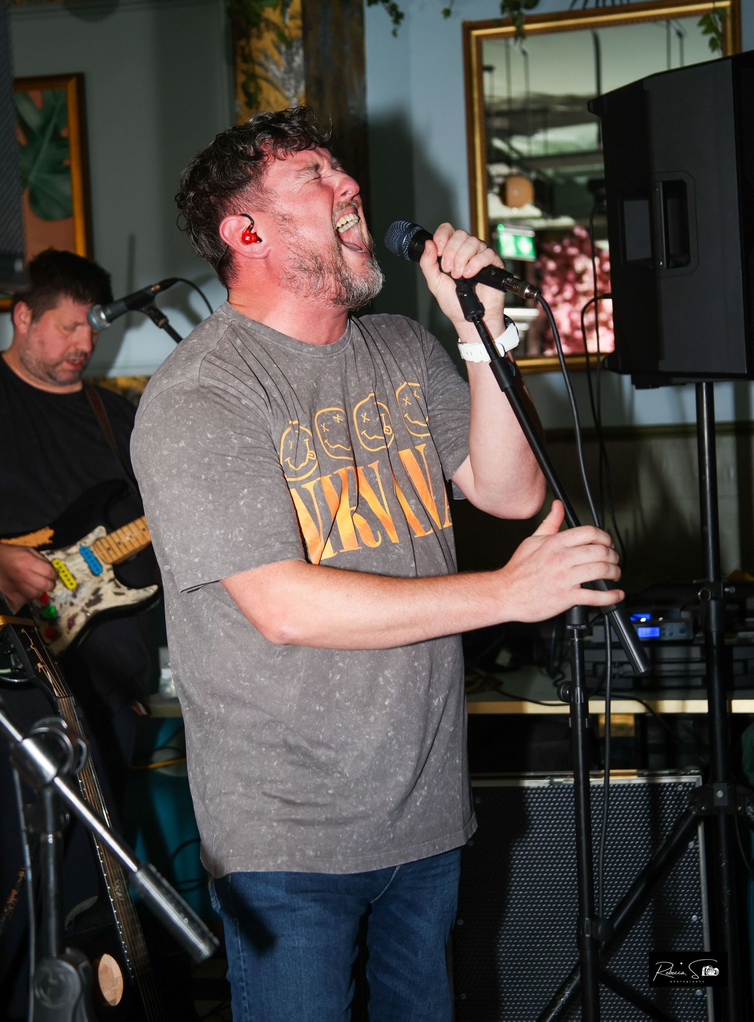 Band performs live on stage with vocalist in grey shirt during indoor concert.