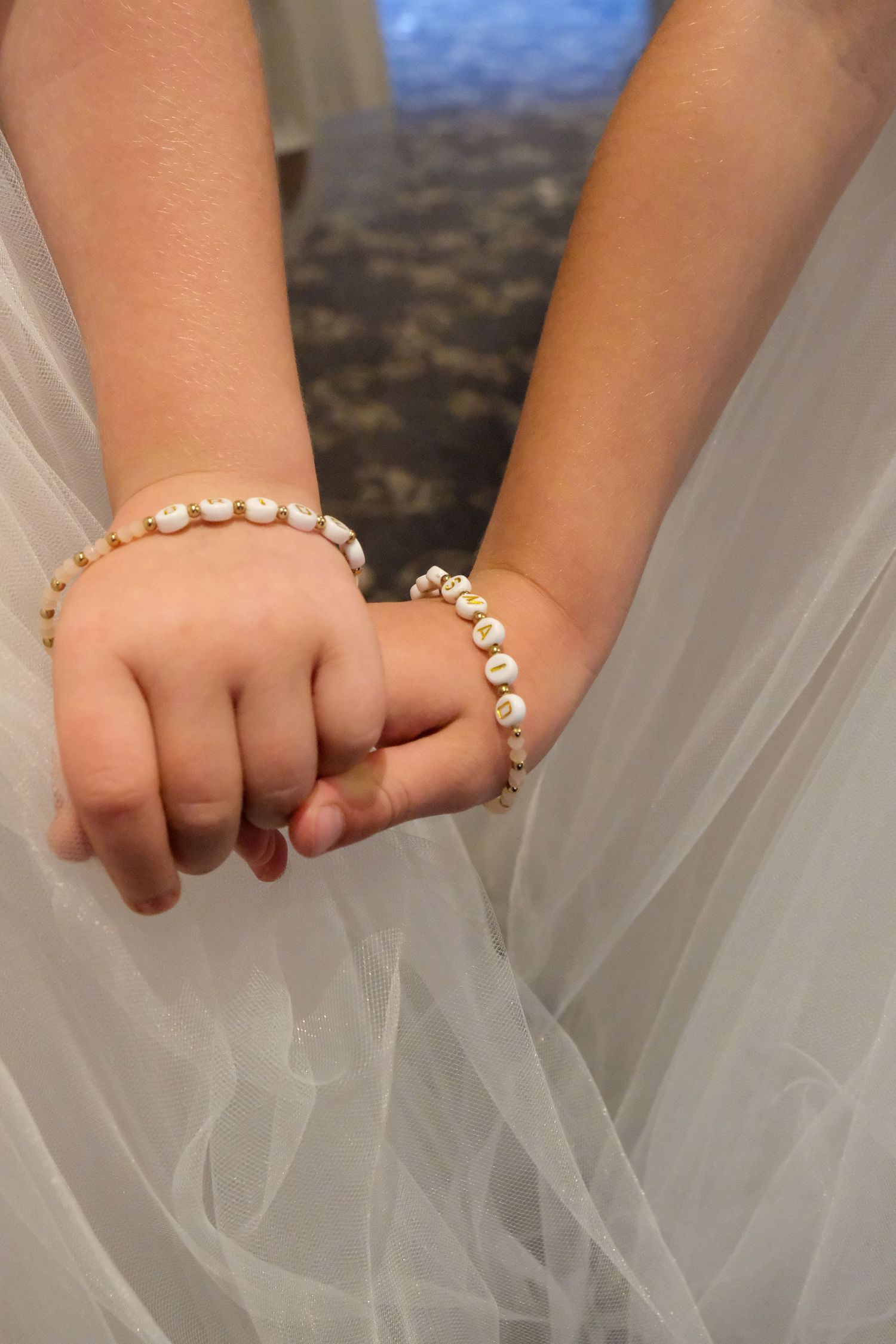Close-up of hands wearing delicate pearl bracelets against white tulle fabric.
