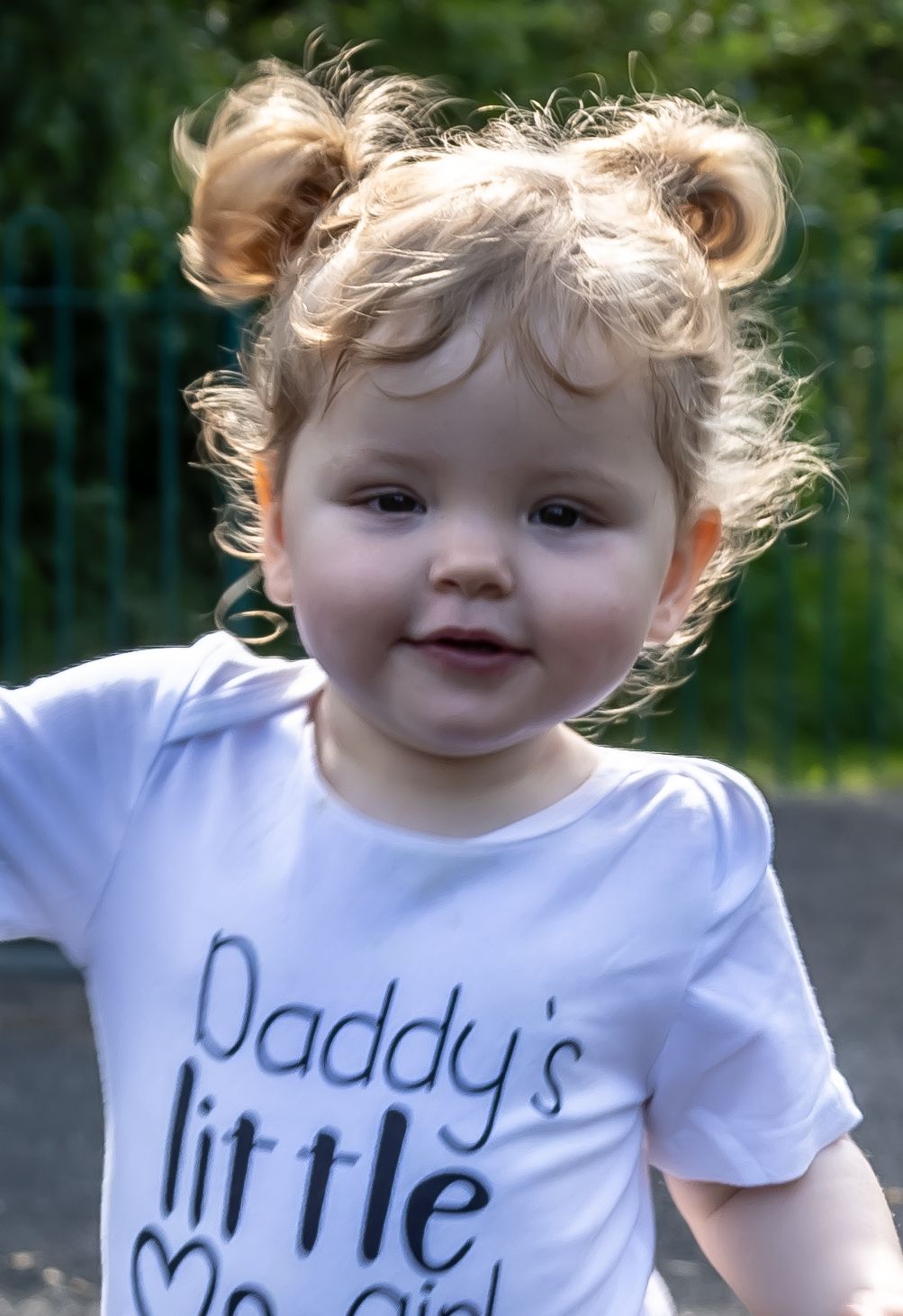 Toddler wearing white t-shirt with text smiling at camera.