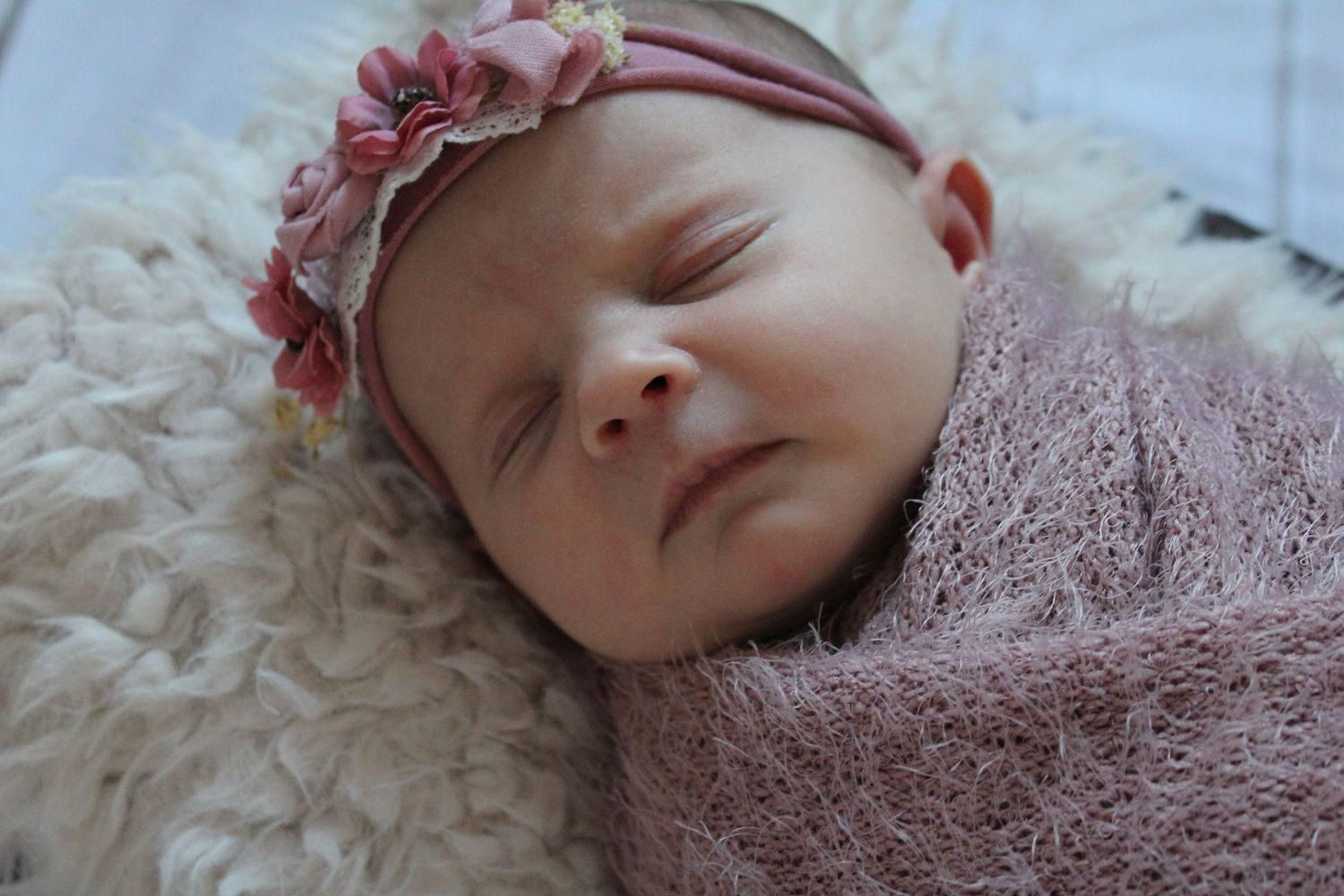 Sleeping baby wrapped in pink blanket with floral headband.