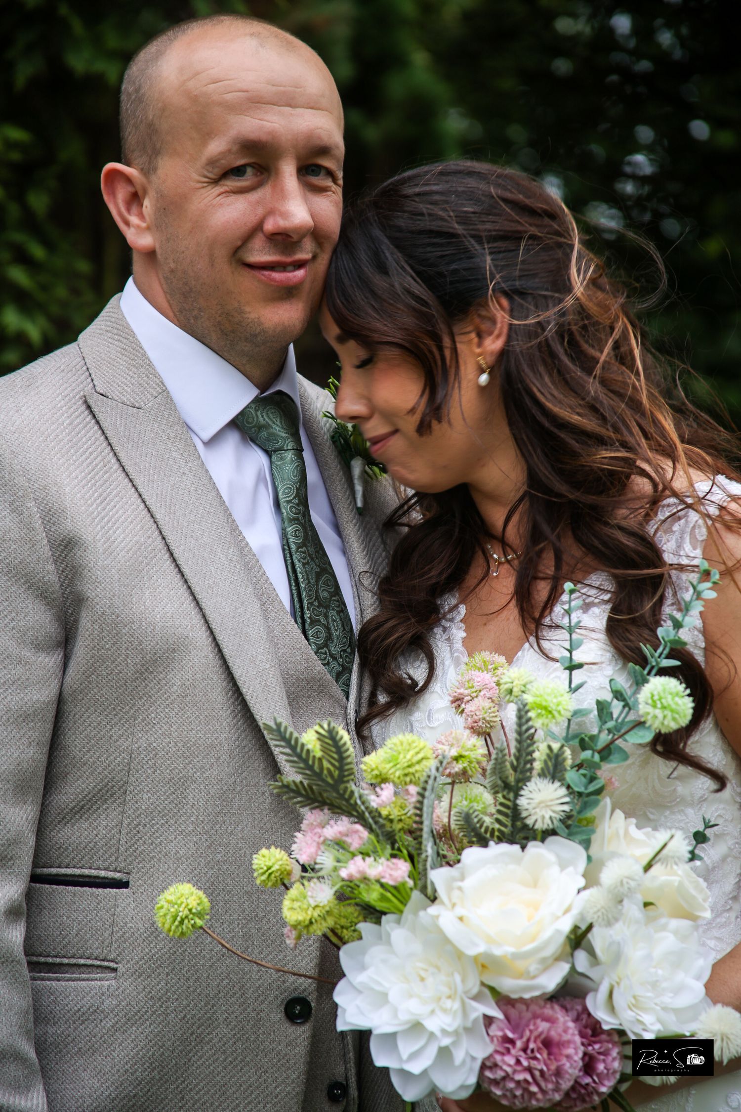 Wedding couple with bouquet of white and pink flowers posing outdoors.