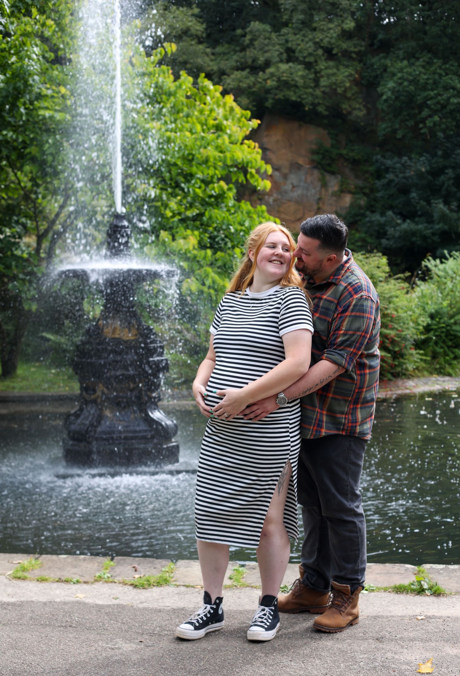 Romantic maternity photoshoot by a fountain in a park setting.
