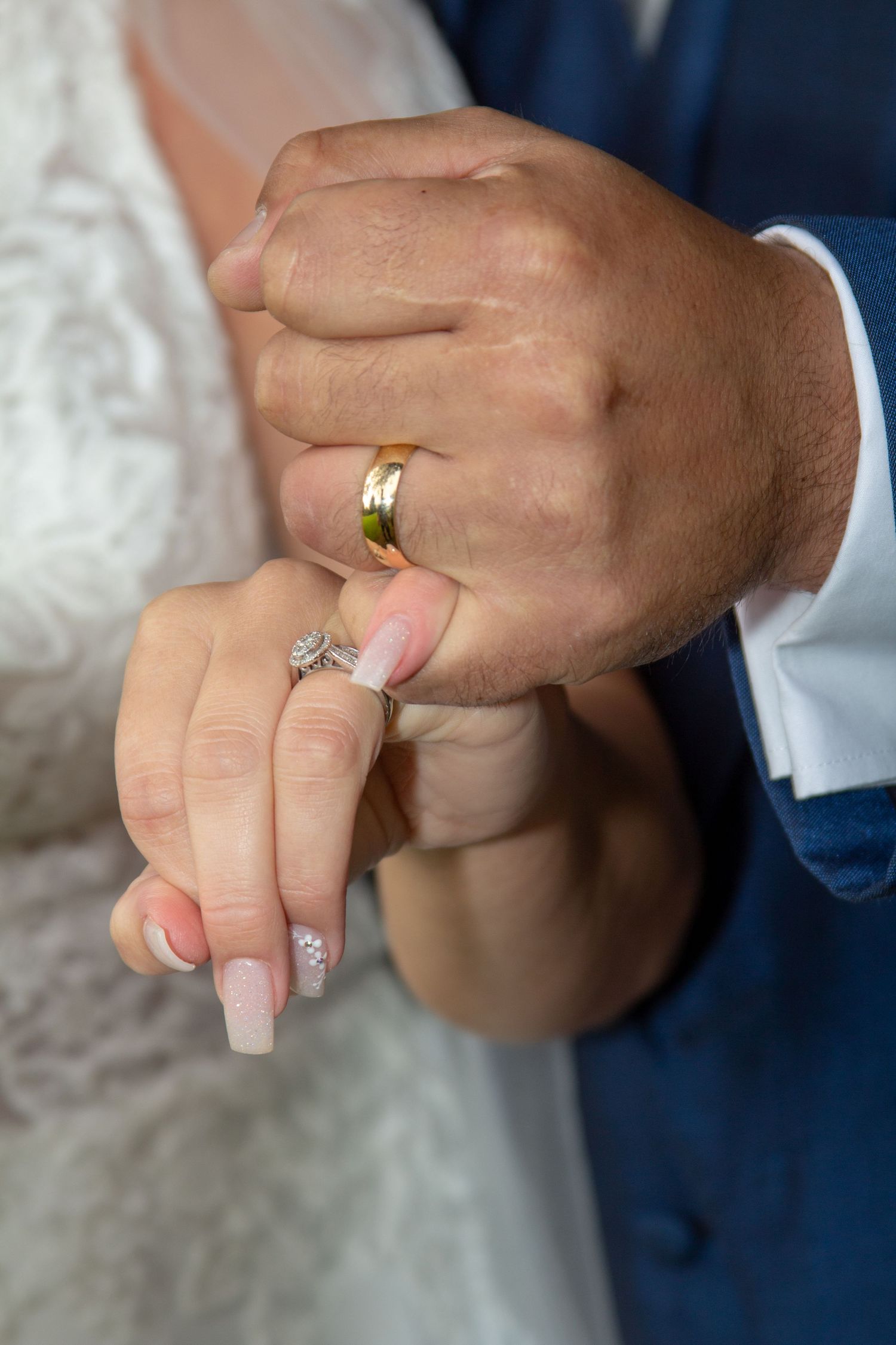 Close-up of wedding rings and manicured hands showing gold band and diamond engagement ring.
