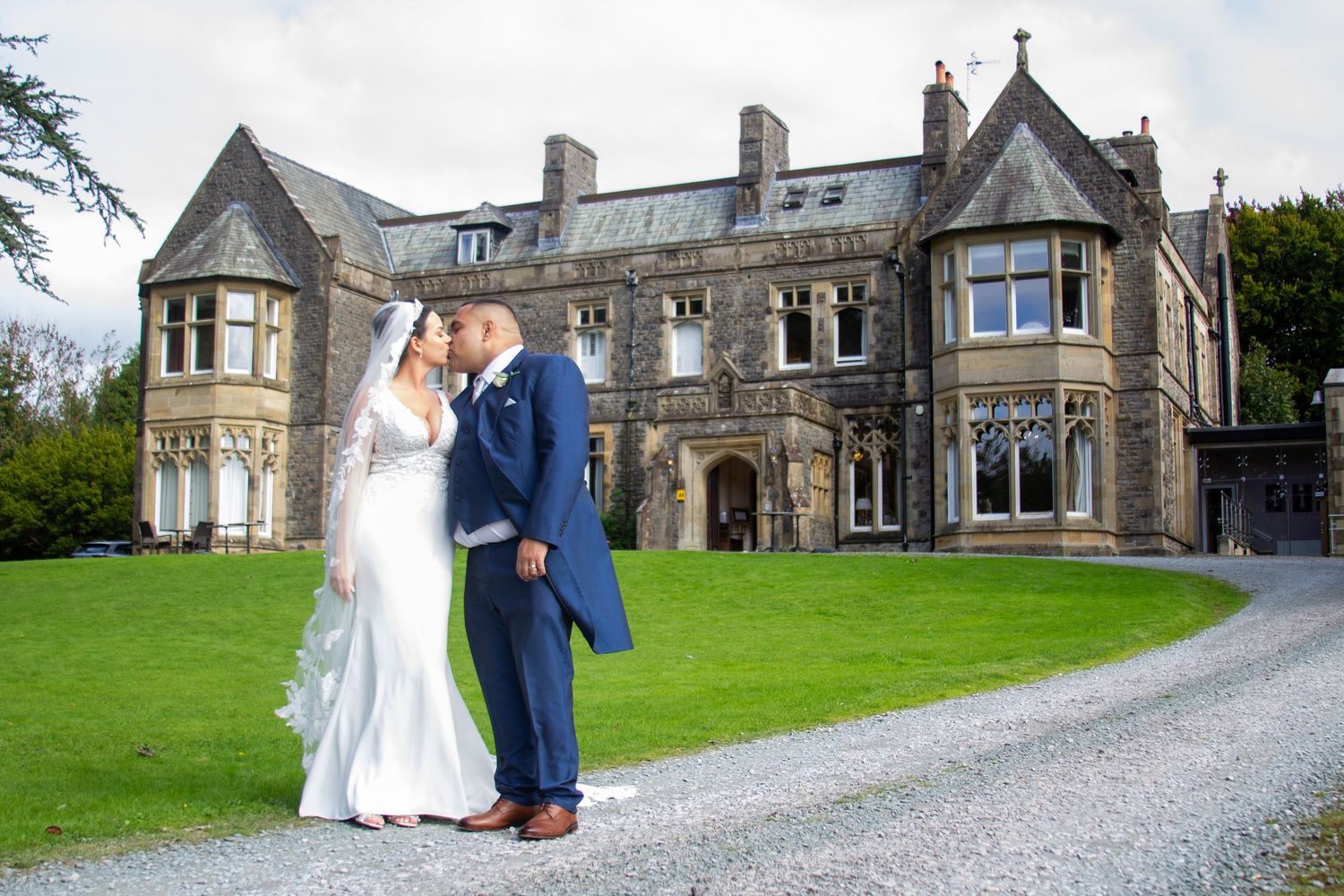 Stone castle wedding venue with gravel driveway and manicured lawn on a cloudy day.