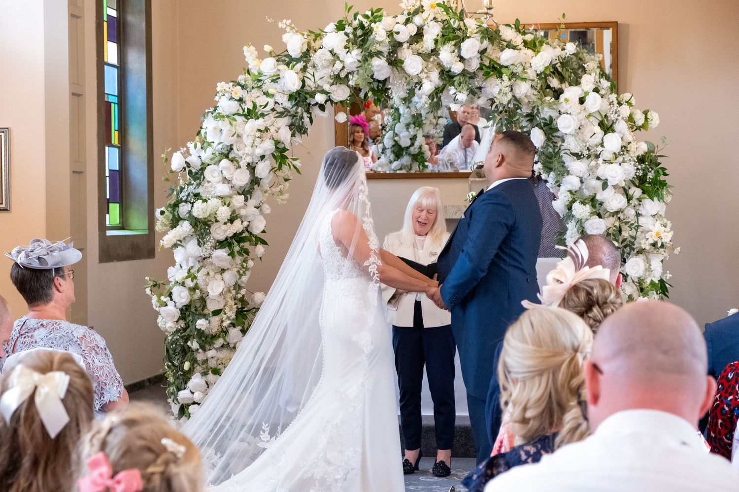 Wedding ceremony scene with elegant white floral arch decorations and guests in attendance.