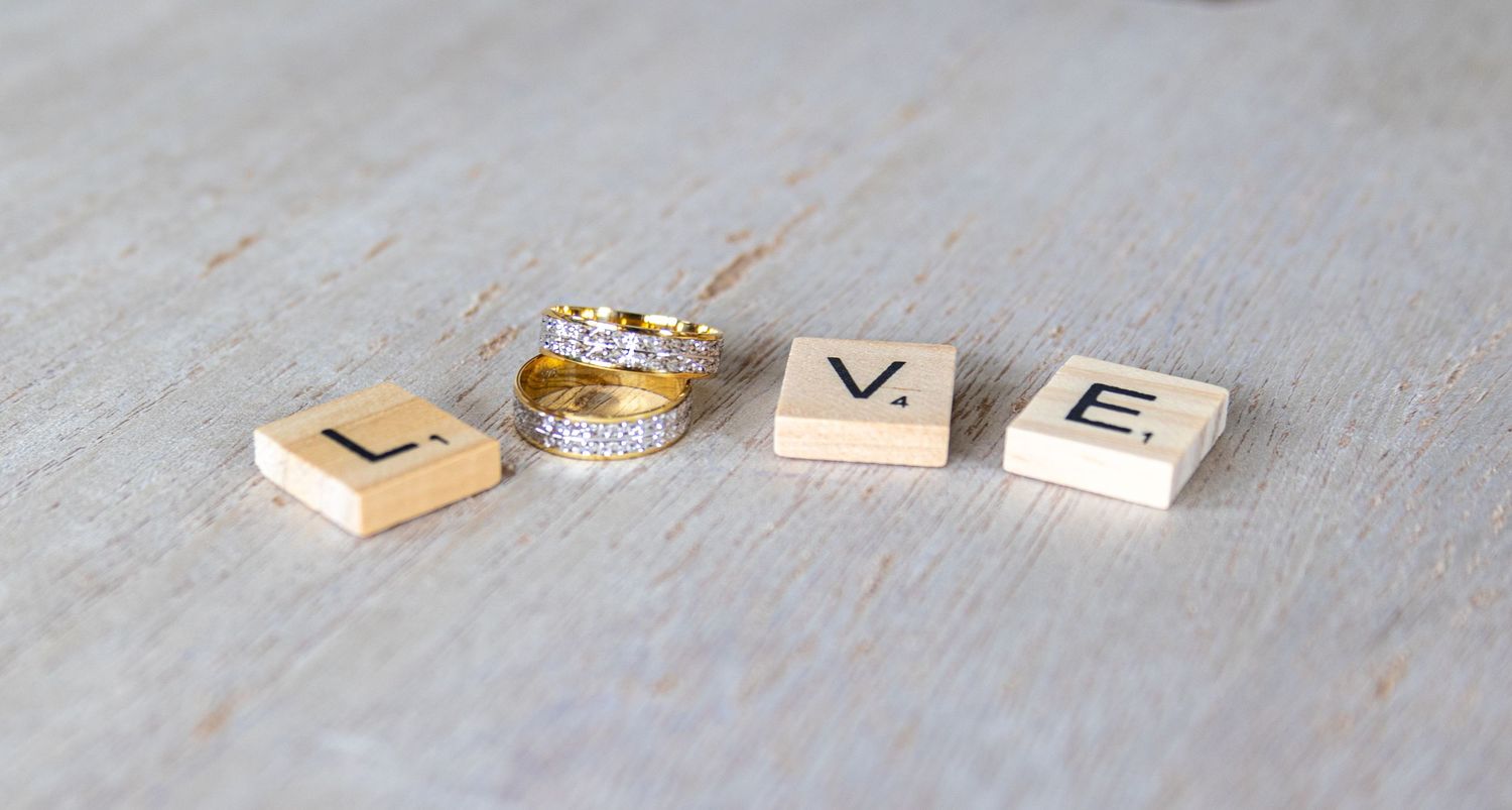 Wedding rings and wooden letter blocks spelling LOVE on light gray surface.