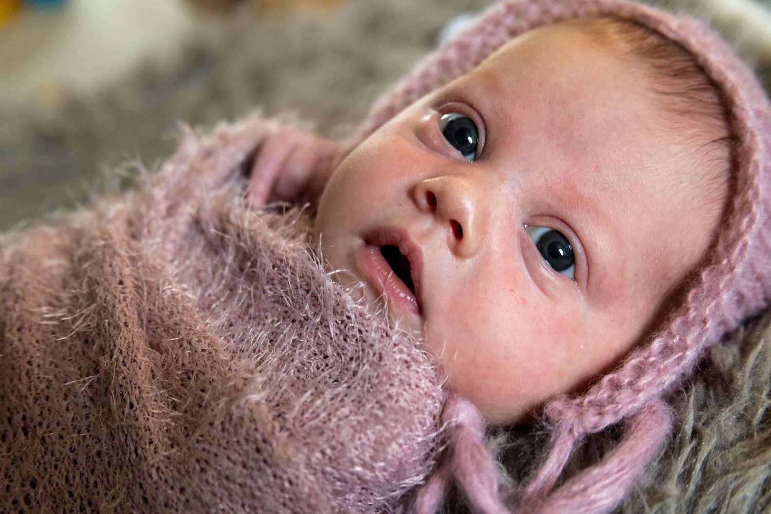 Close-up portrait of baby wearing pink knit hat against dark background.