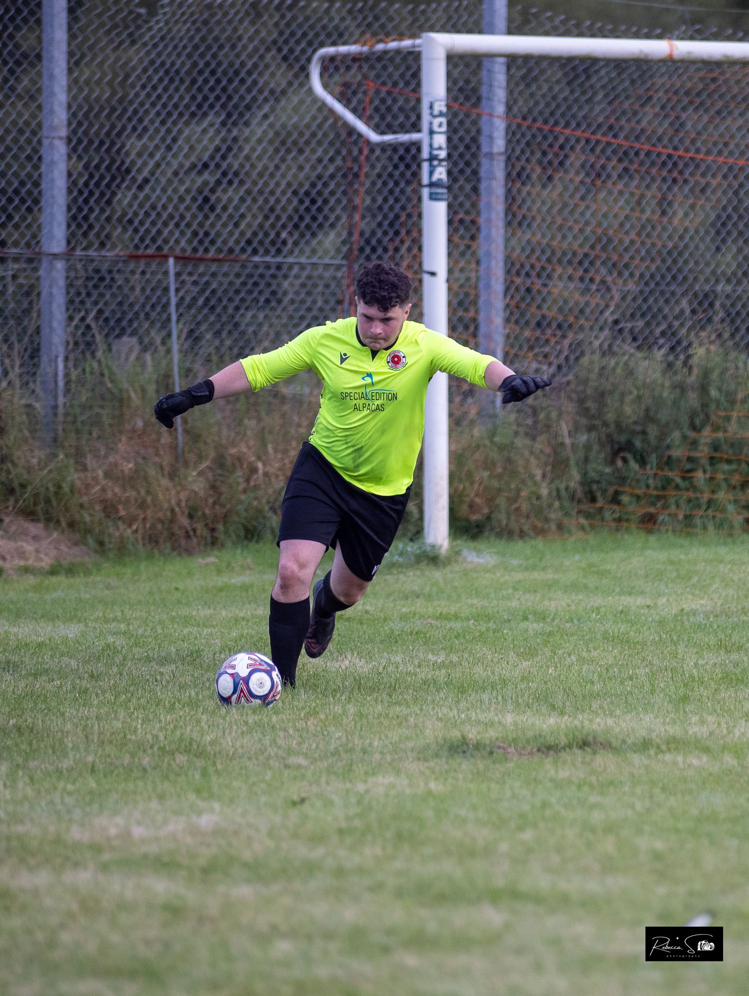 Goalkeeper in yellow uniform preparing to kick soccer ball on field.