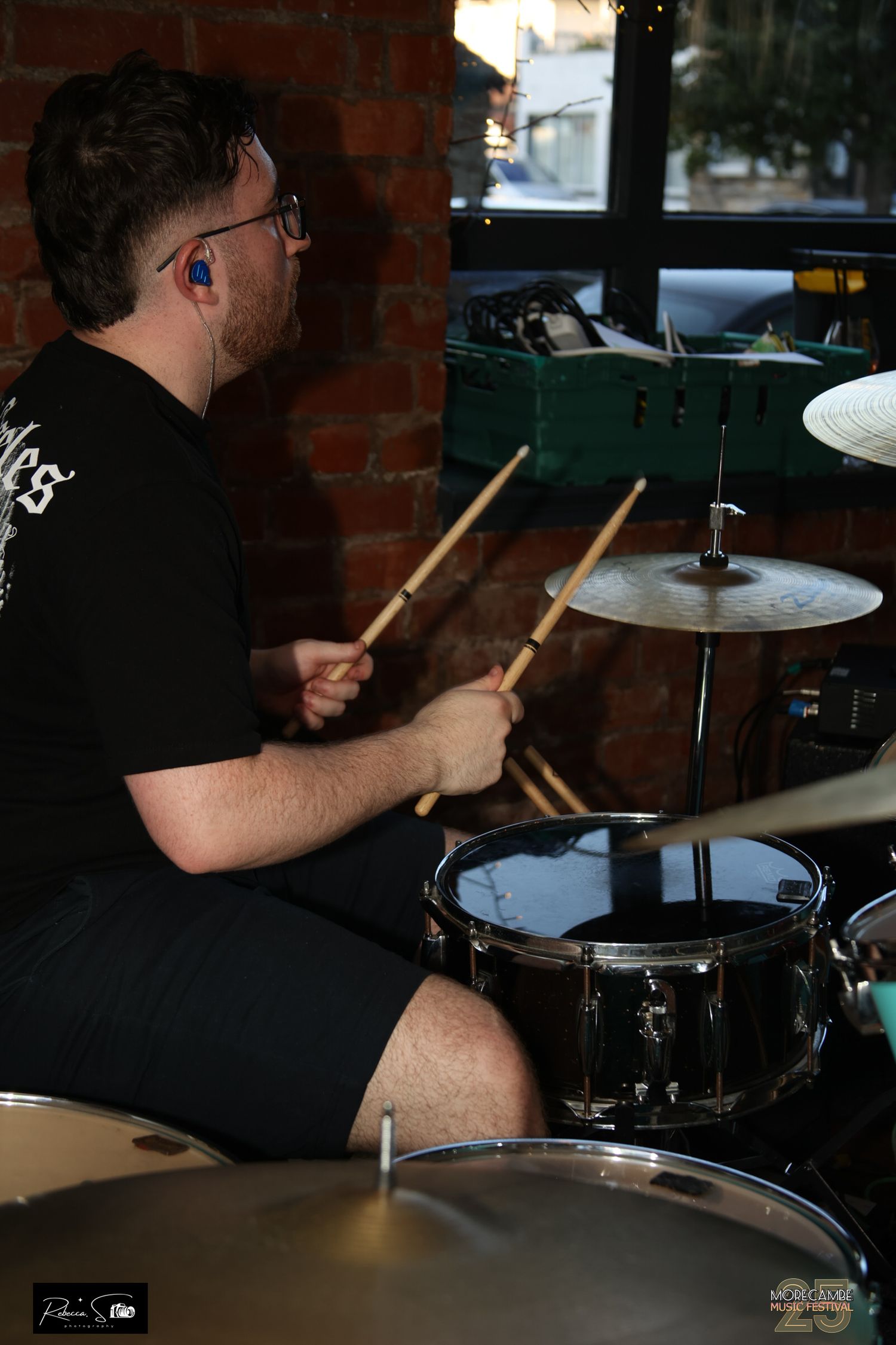 Drummer performs behind a drum kit in a brick-walled venue.