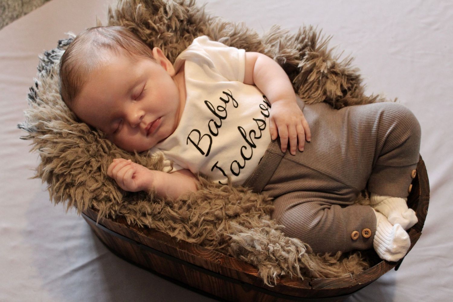Sleeping baby on brown fur blanket wearing beige onesie.