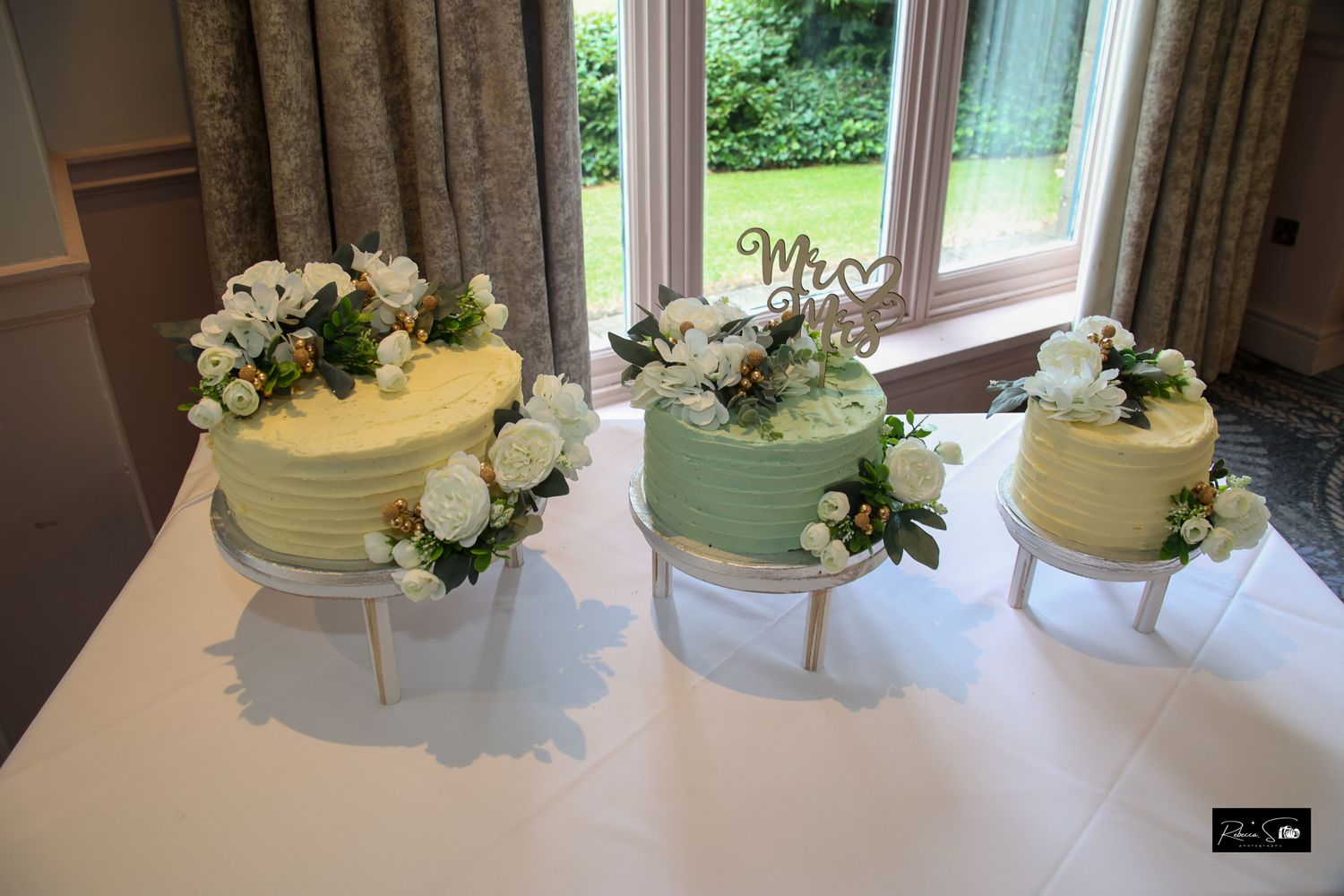 Three-tiered pastel wedding cake decorated with fresh flowers on white tablecloth.